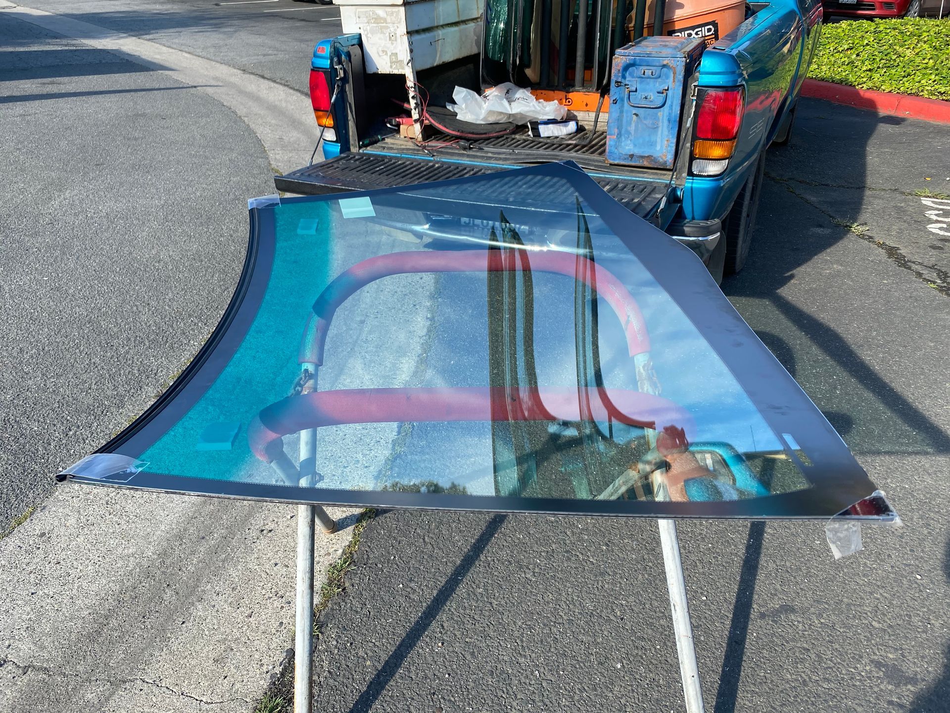 Windshield leaning on a stand, next to a pickup truck. The windshield is blue-tinted.