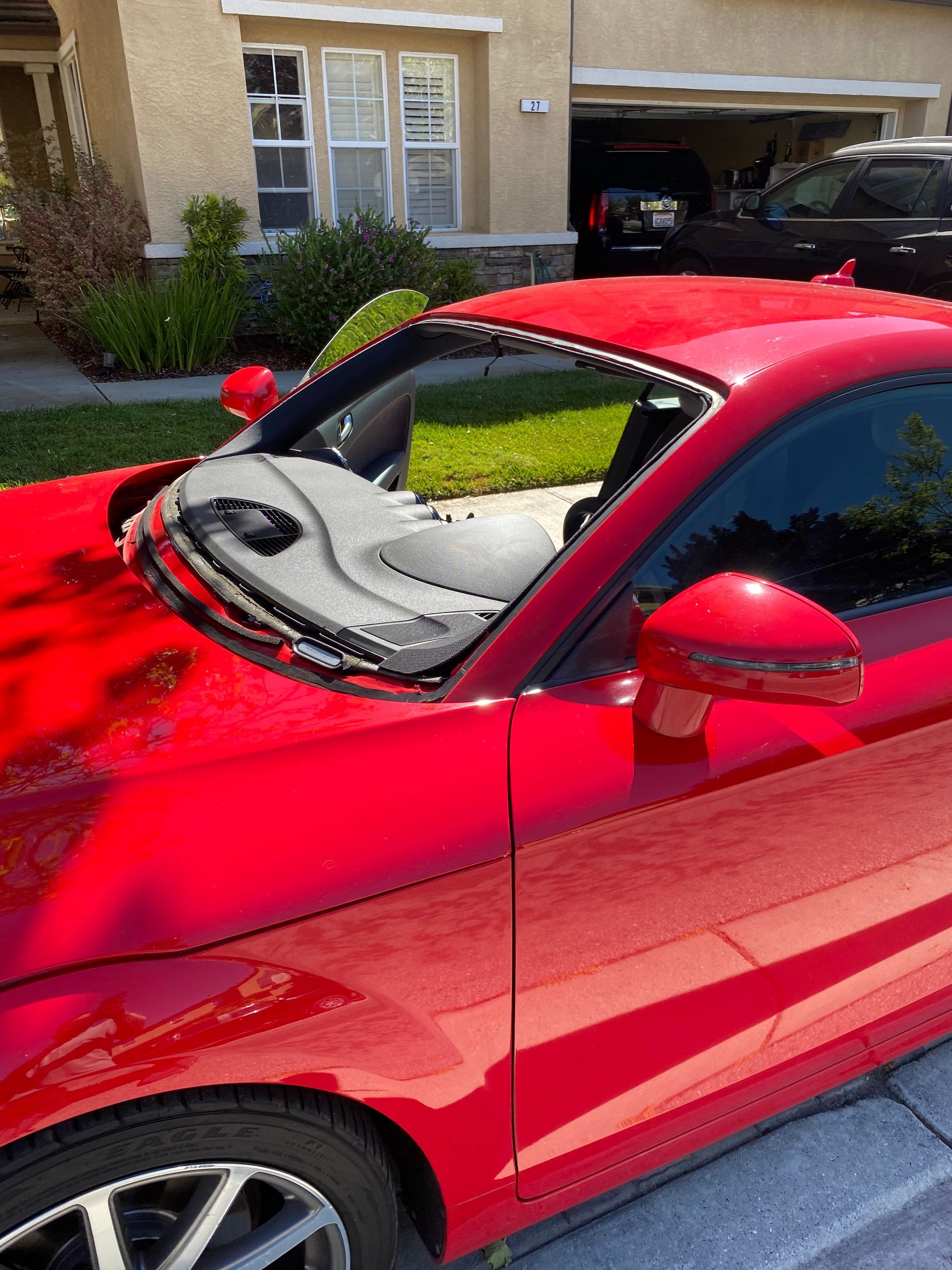 Red car with damaged windshield parked on a sunny residential street.