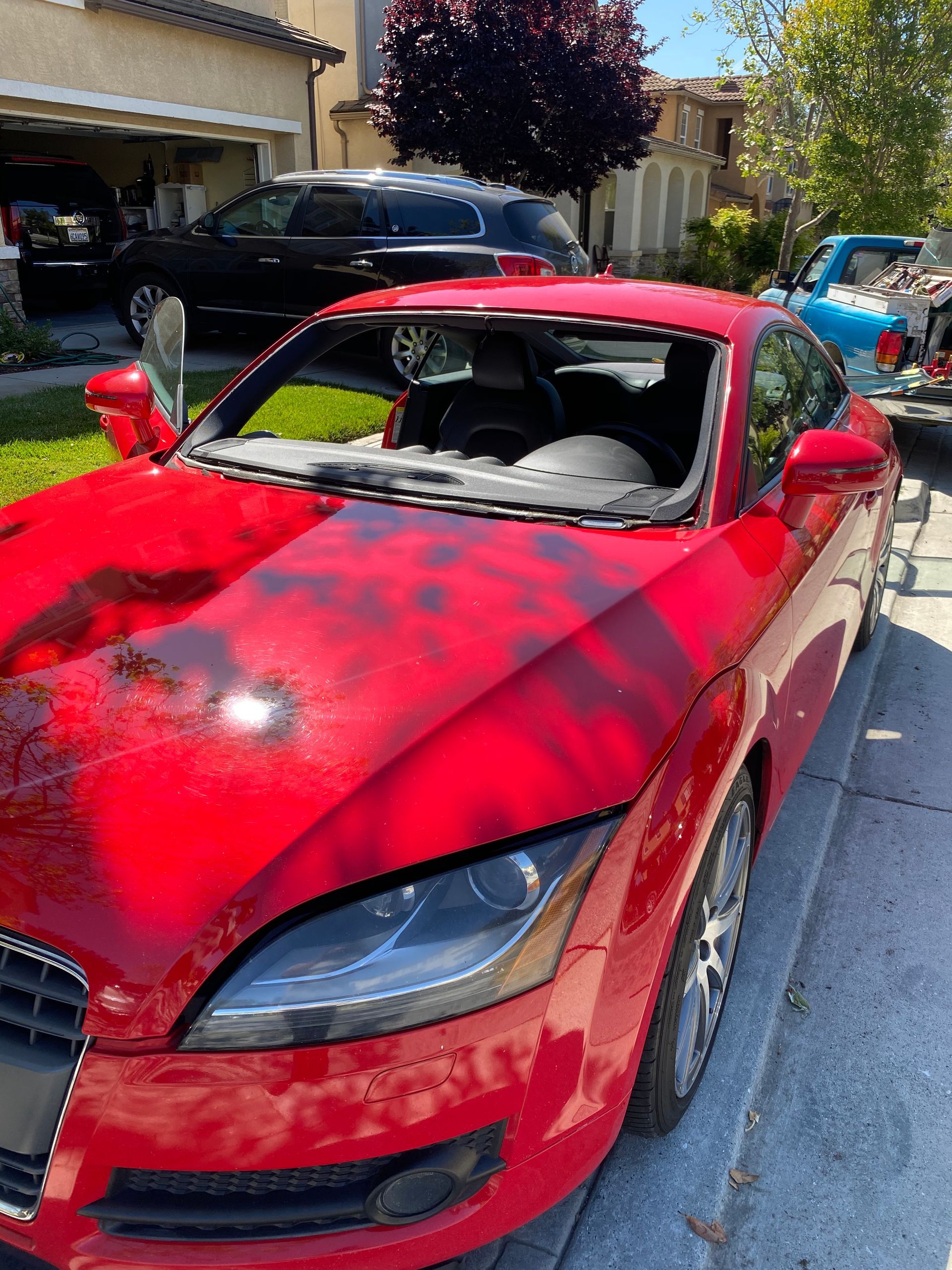 Red Audi TT coupe with a damaged windshield parked on a street in front of a house.