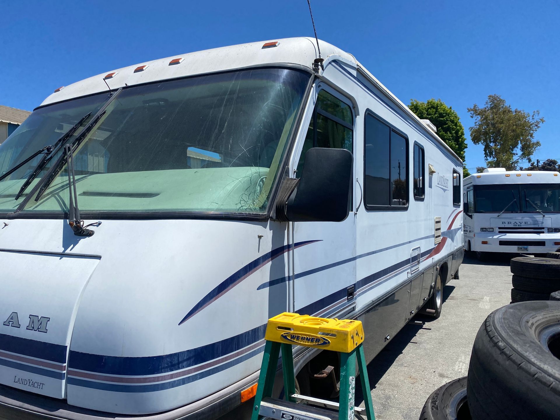 White RV with blue and red stripes, parked outside, sunny day.