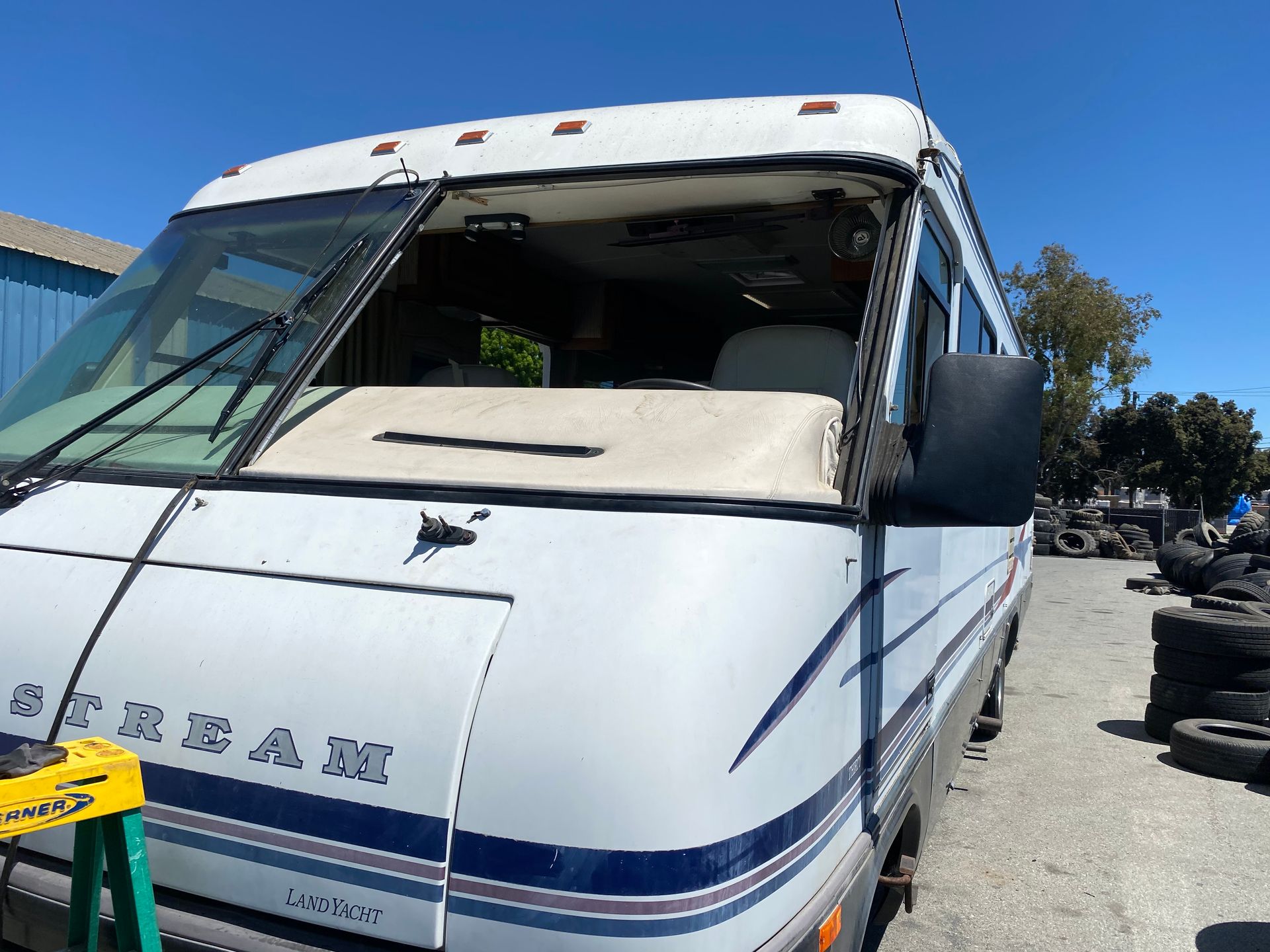 White Sunstream RV with missing windshield parked outside, sunny day.