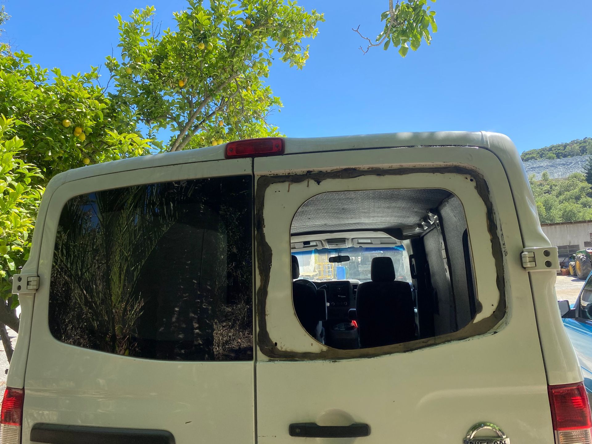 Rear of a white van with a missing window, exposing the interior. The remaining window is visible.