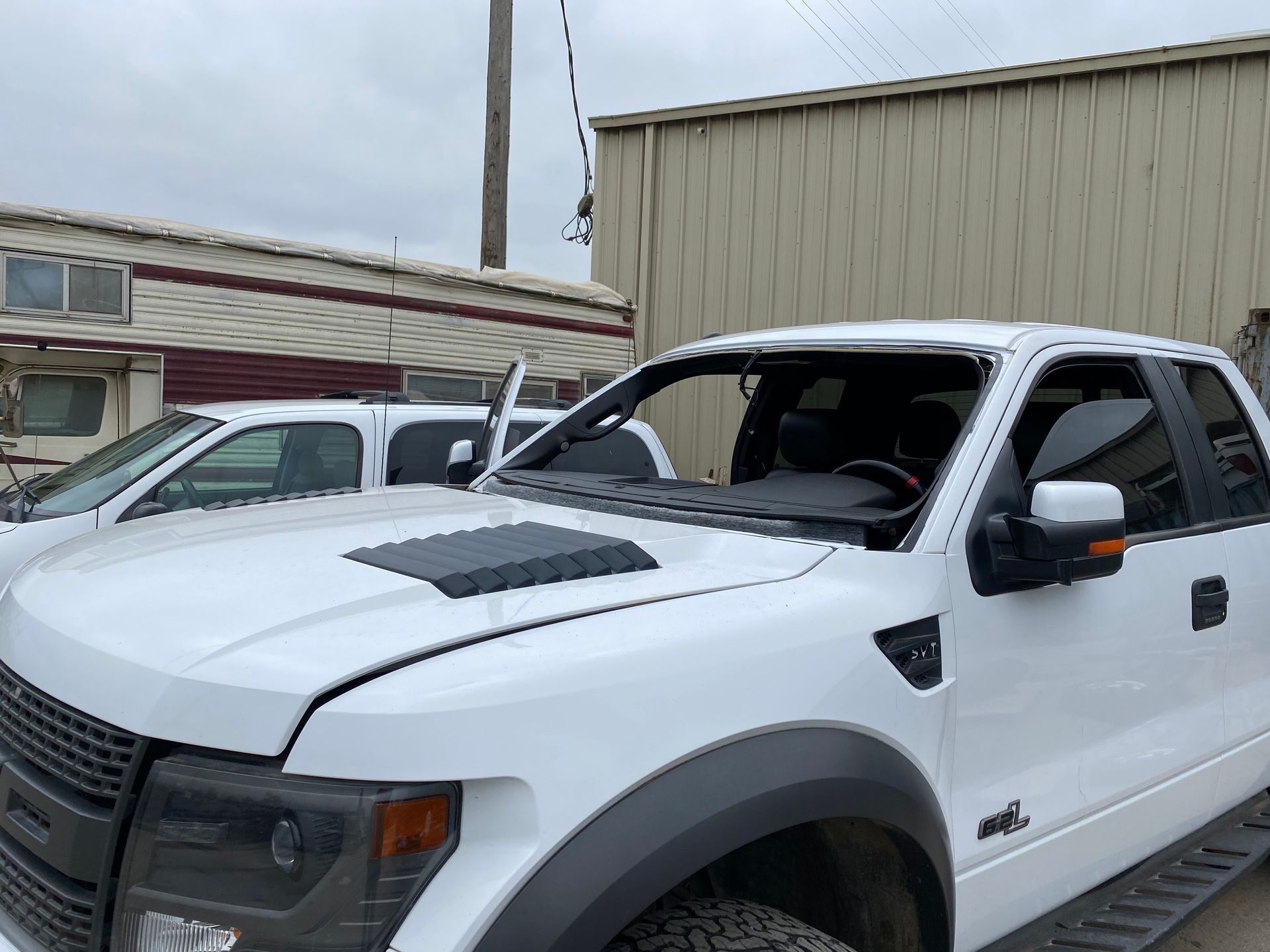 White Ford Raptor truck with windshield removed, parked outside a building.