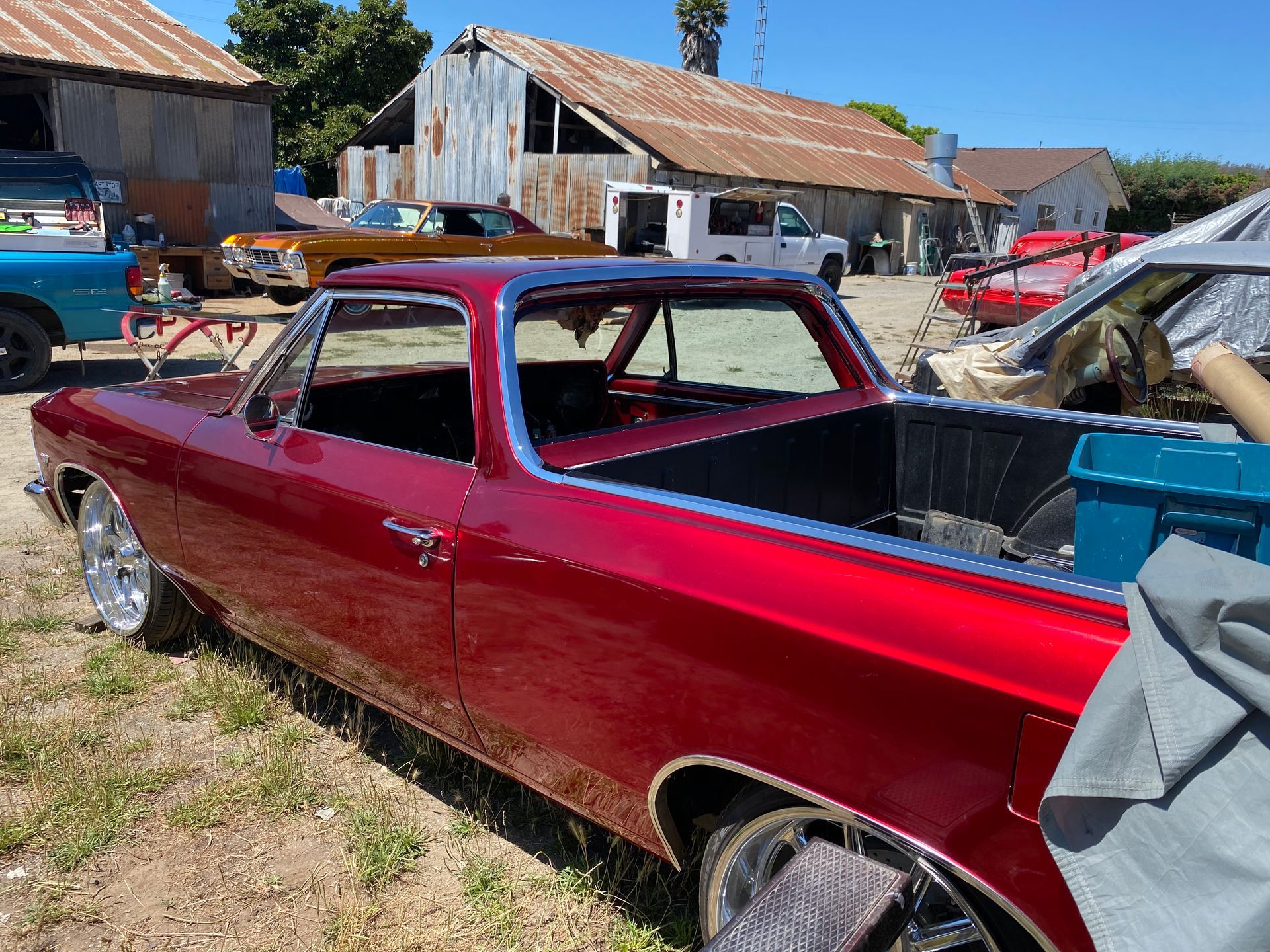 Red classic Chevrolet El Camino truck parked outdoors near a barn, other vehicles visible.