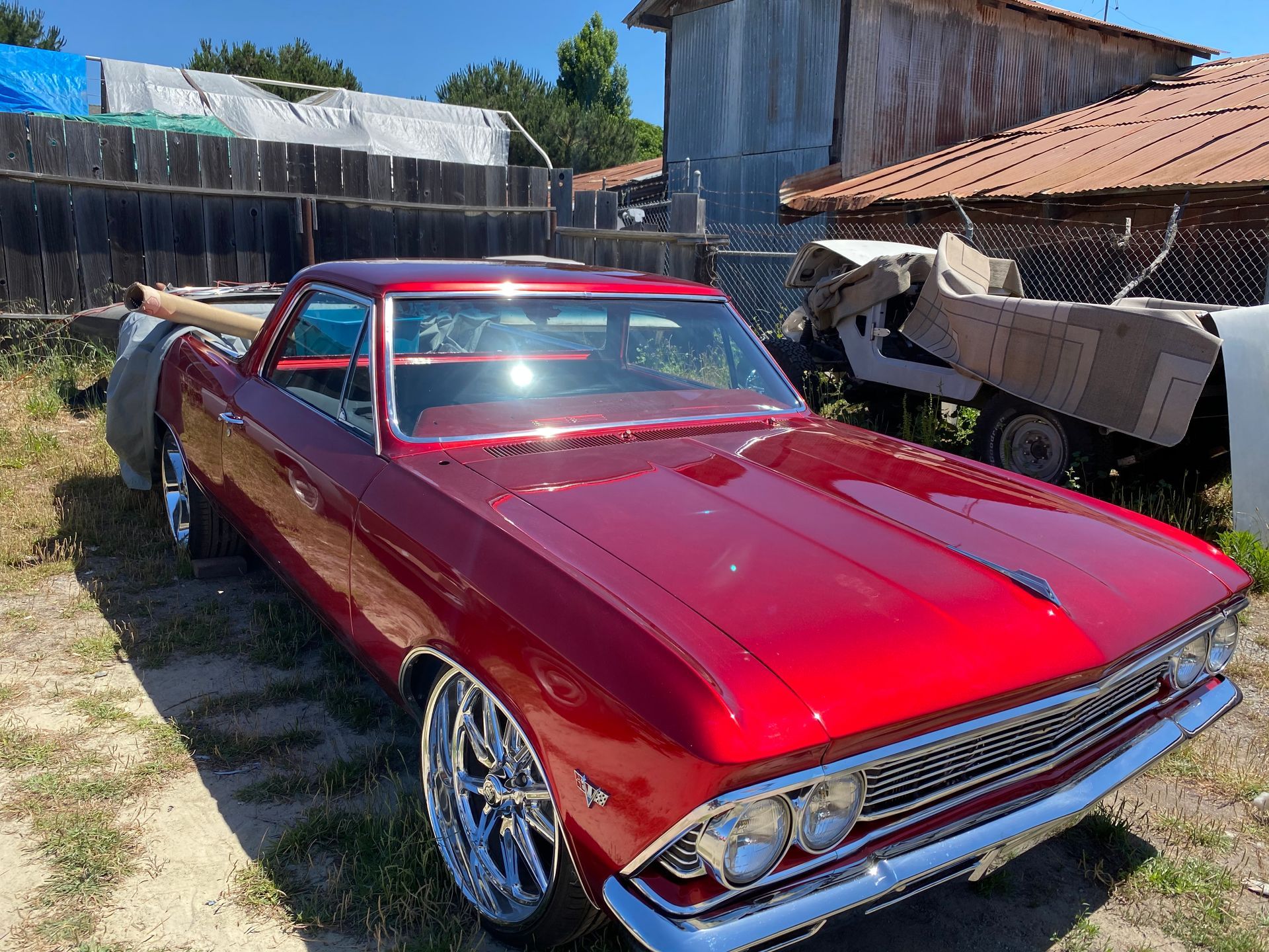 Red classic Chevrolet El Camino truck with chrome wheels parked outdoors.