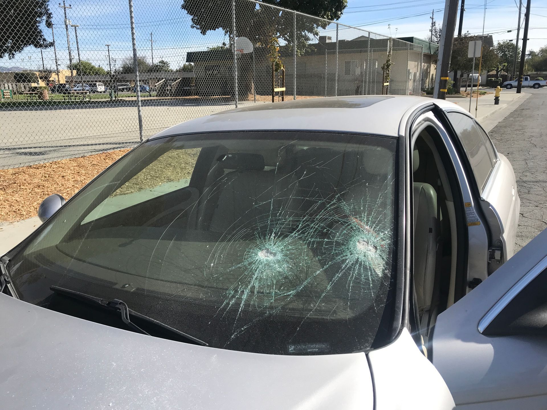 Silver car windshield with multiple impact points, door open, parked on a street.