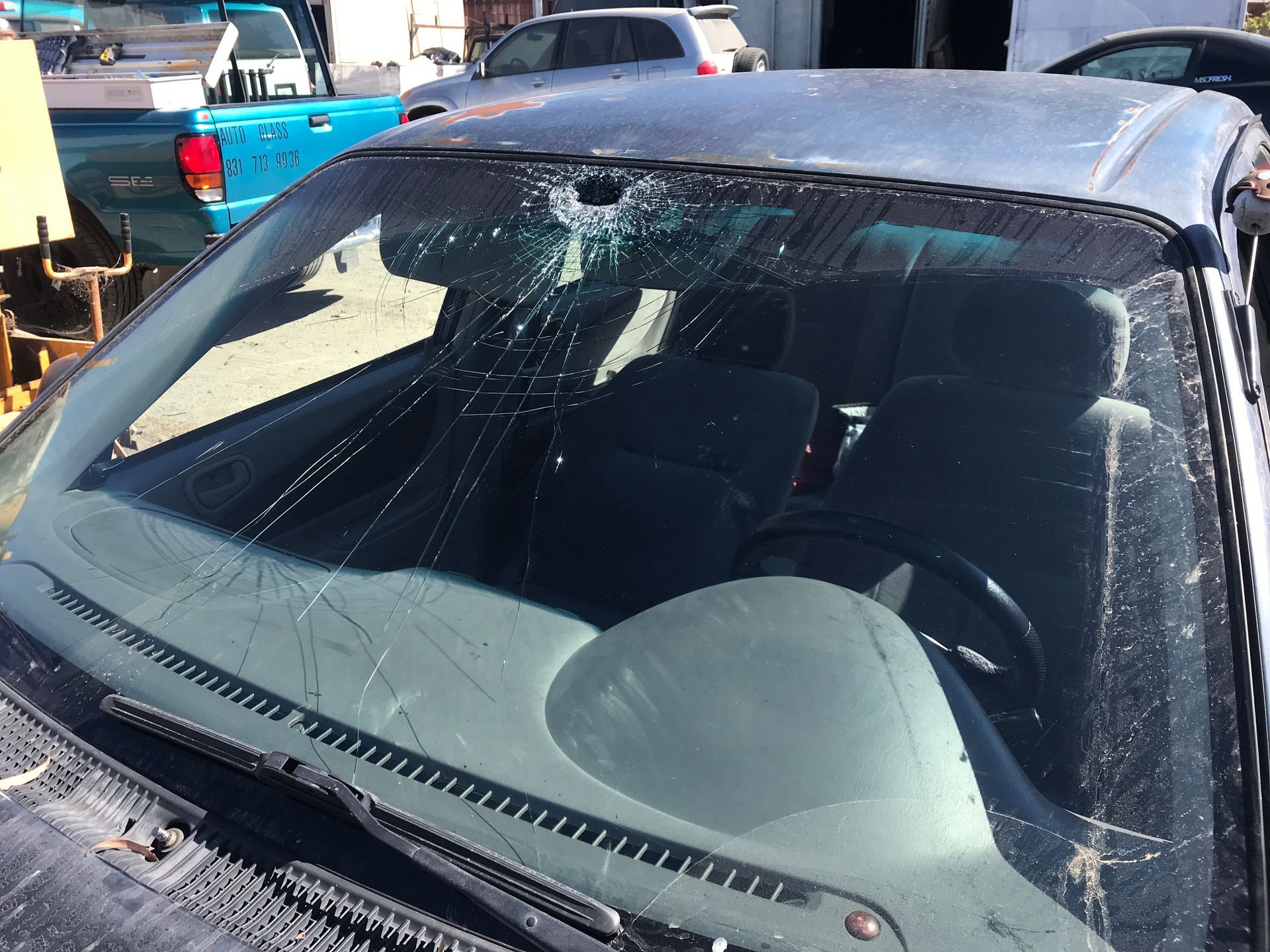 A car with a severely cracked windshield, viewed from the front, in a junkyard setting.