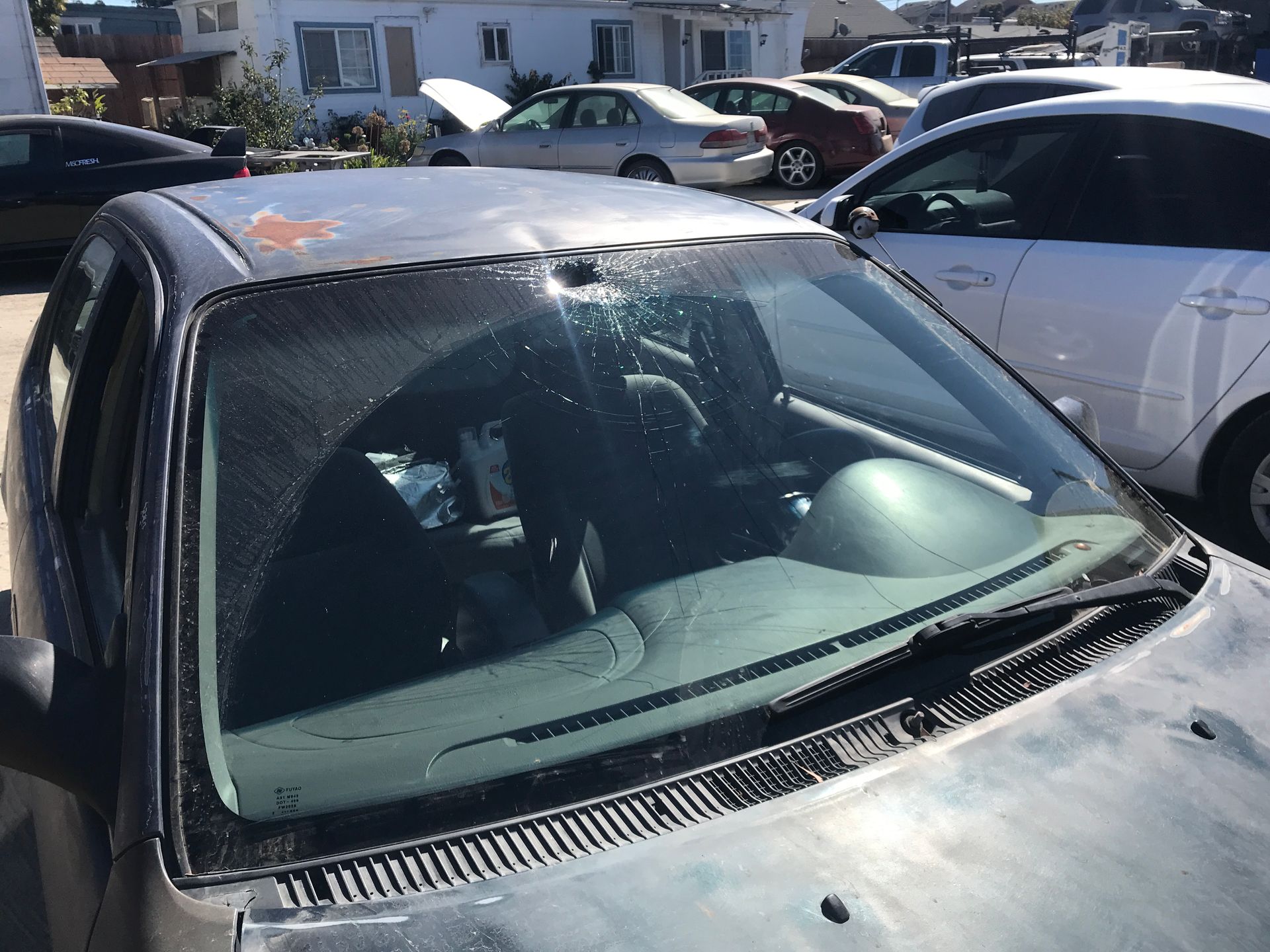 Close-up of a damaged car's windshield and roof with other parked cars in the background.
