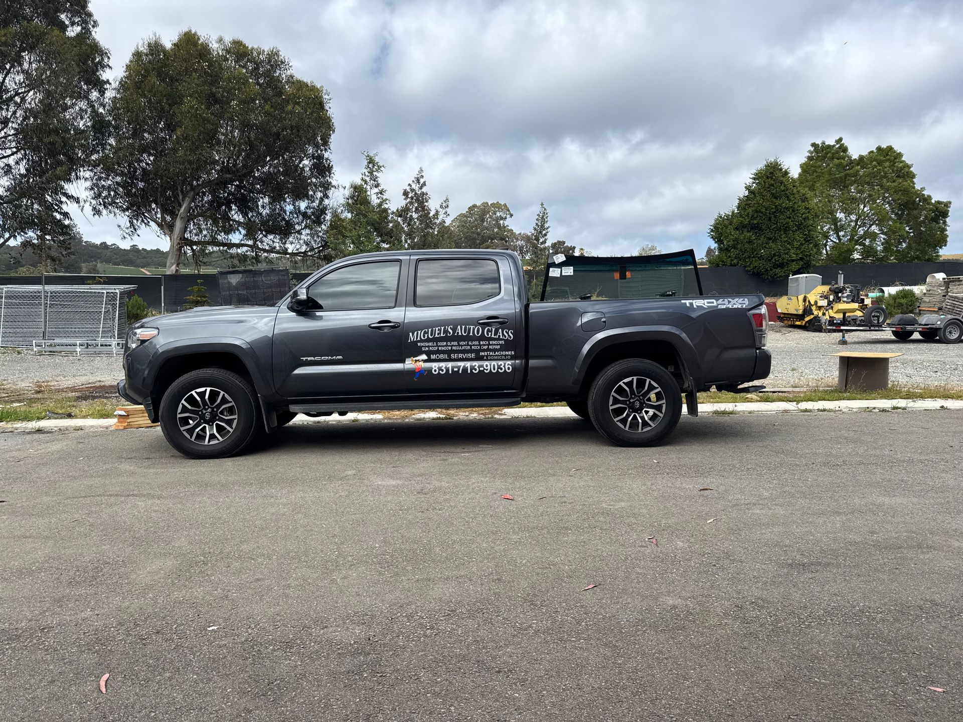 Gray Toyota Tacoma truck parked on asphalt. Side view with company logo. Cloudy sky background.