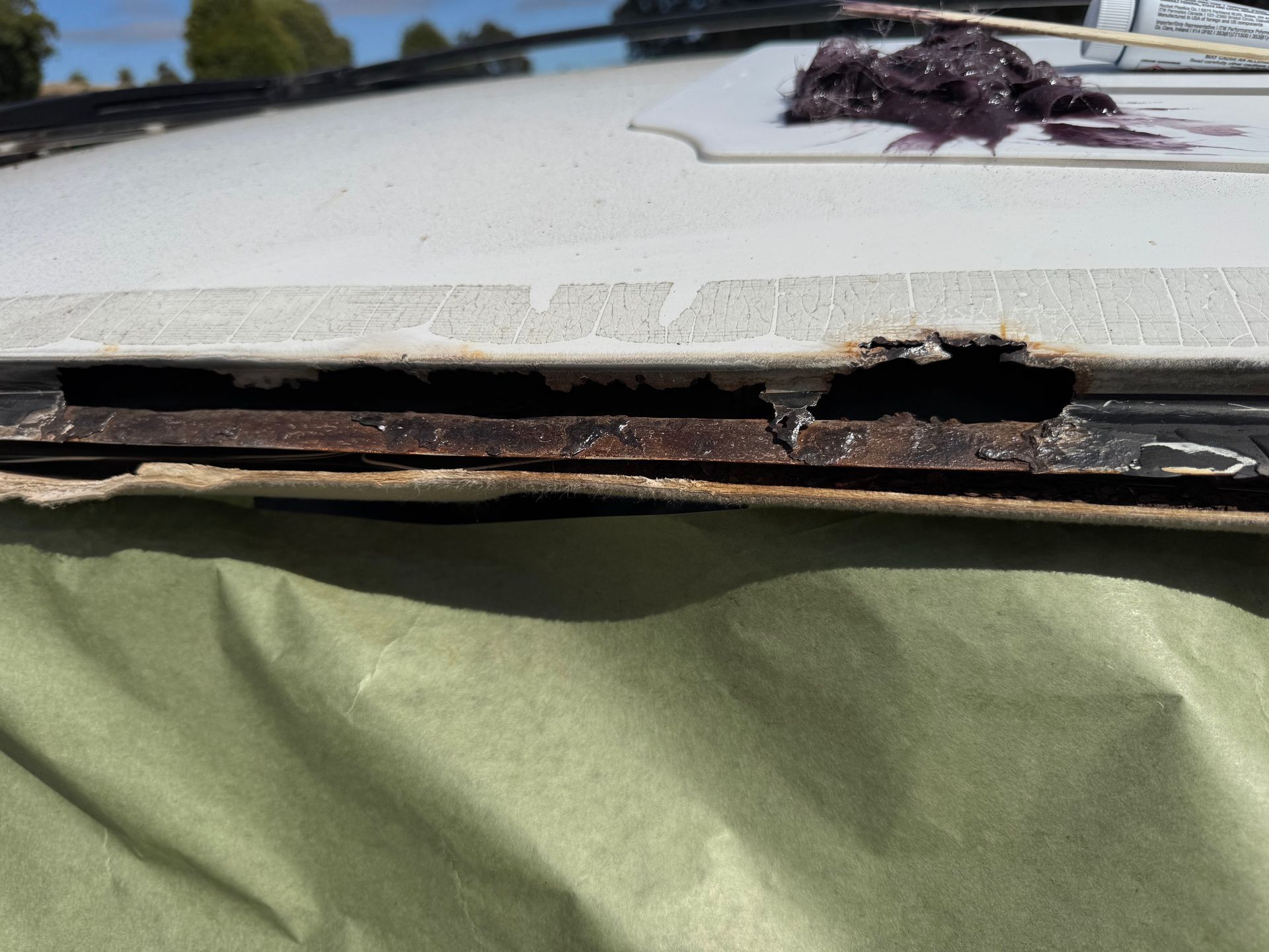 Rust on a vehicle roof edge, with visible metal and debris. White paint is chipped.
