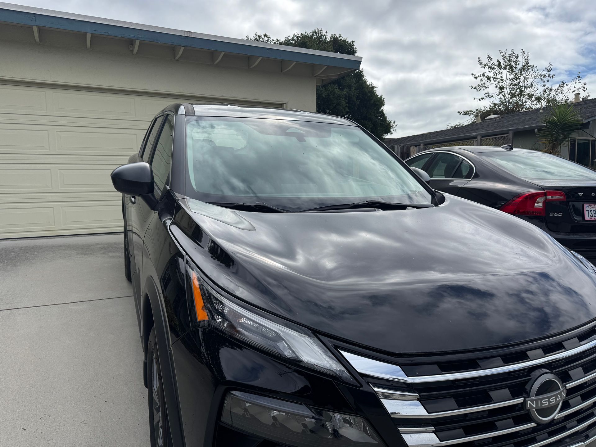 Black Nissan SUV parked in front of a garage, with a second car visible in the background on a cloudy day.