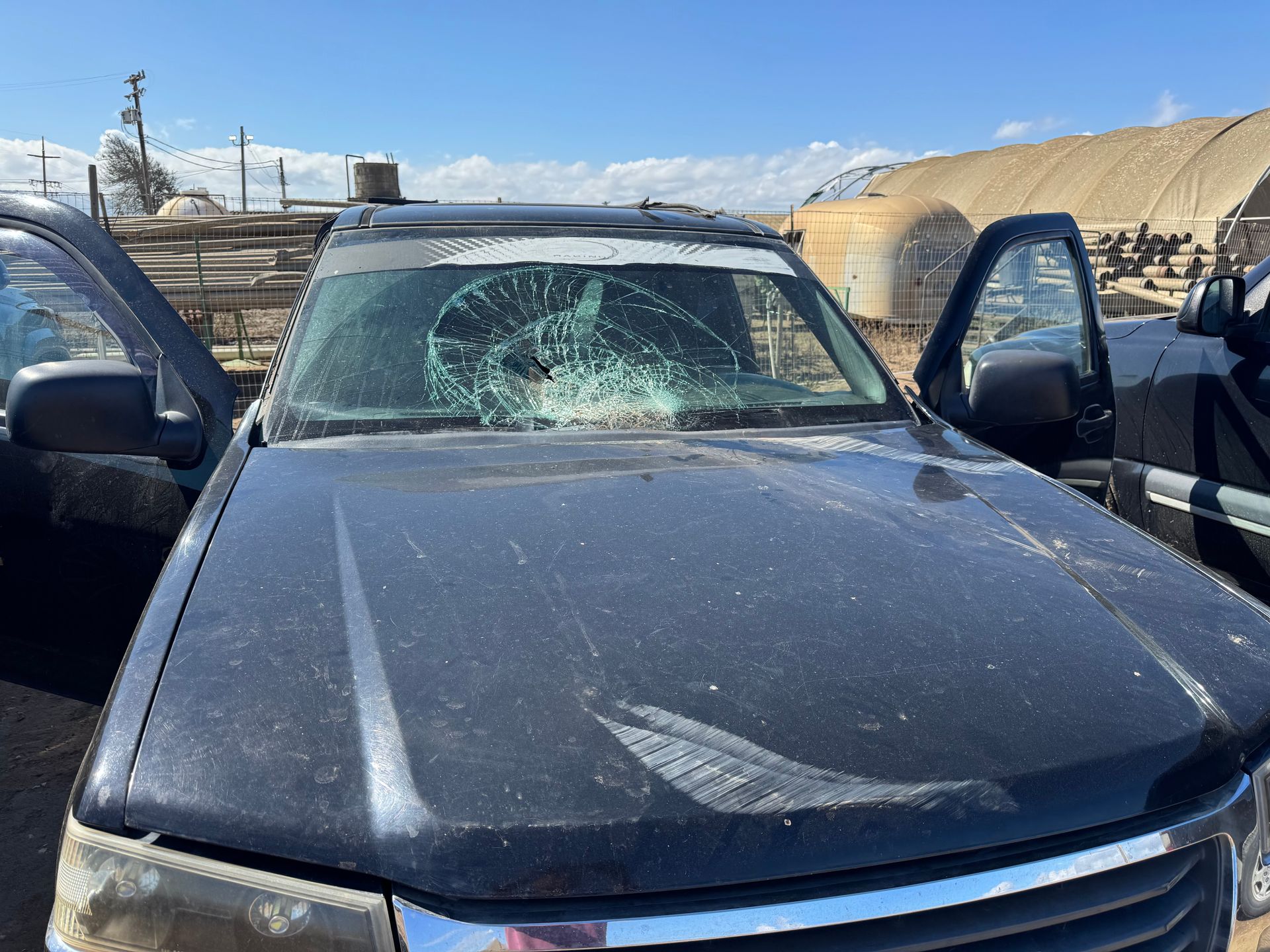 Black SUV with shattered windshield and open door, parked outdoors in a rural setting.