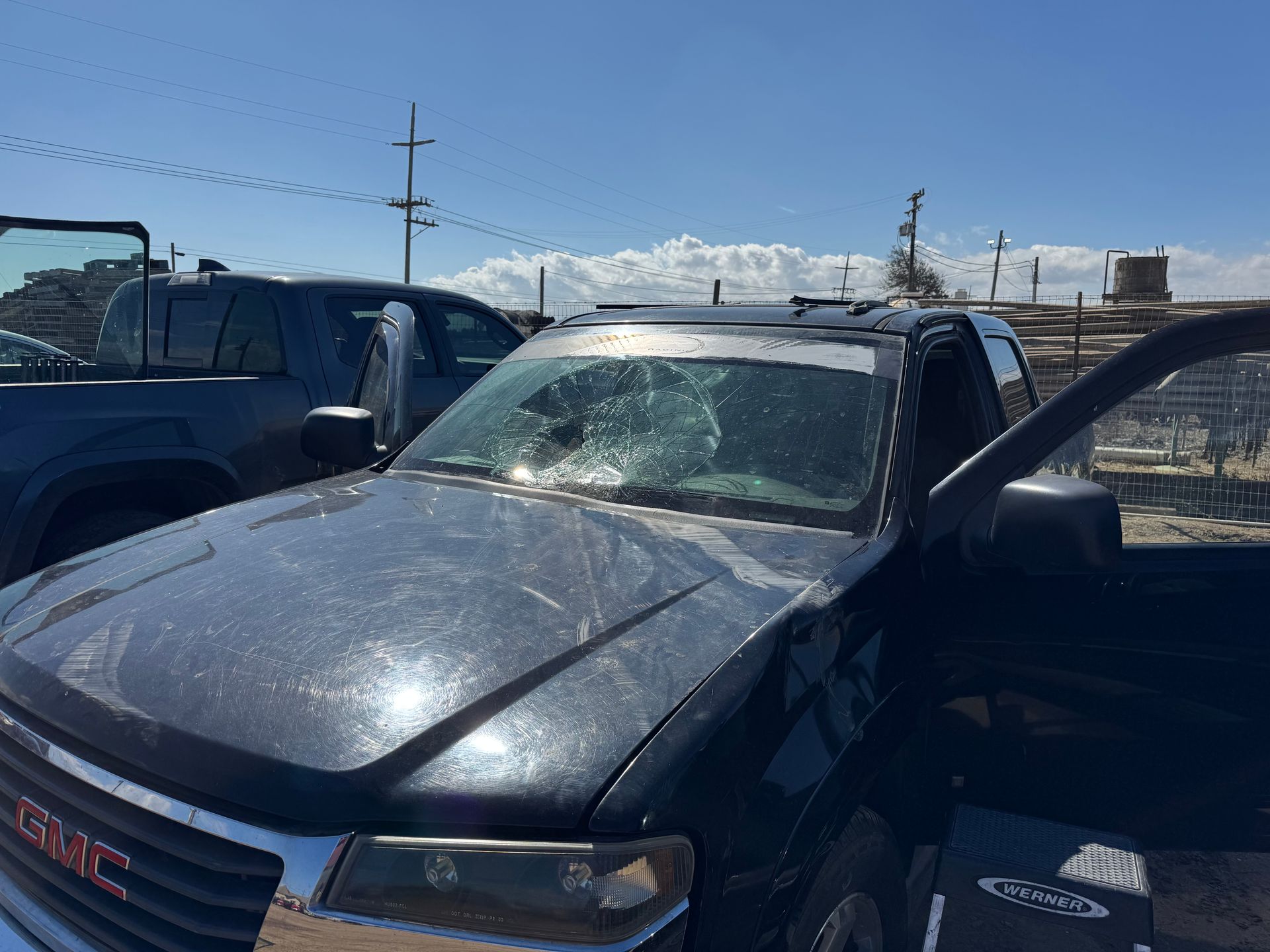 Dark blue GMC truck with shattered windshield and open door parked outside.