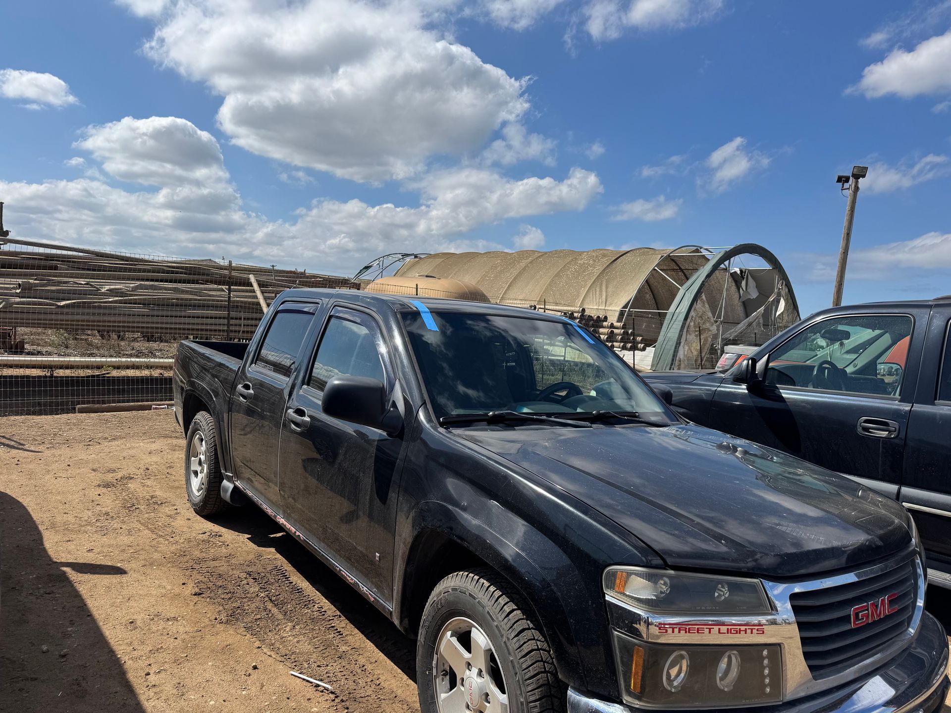 Black GMC truck parked in a dirt lot under a cloudy sky.