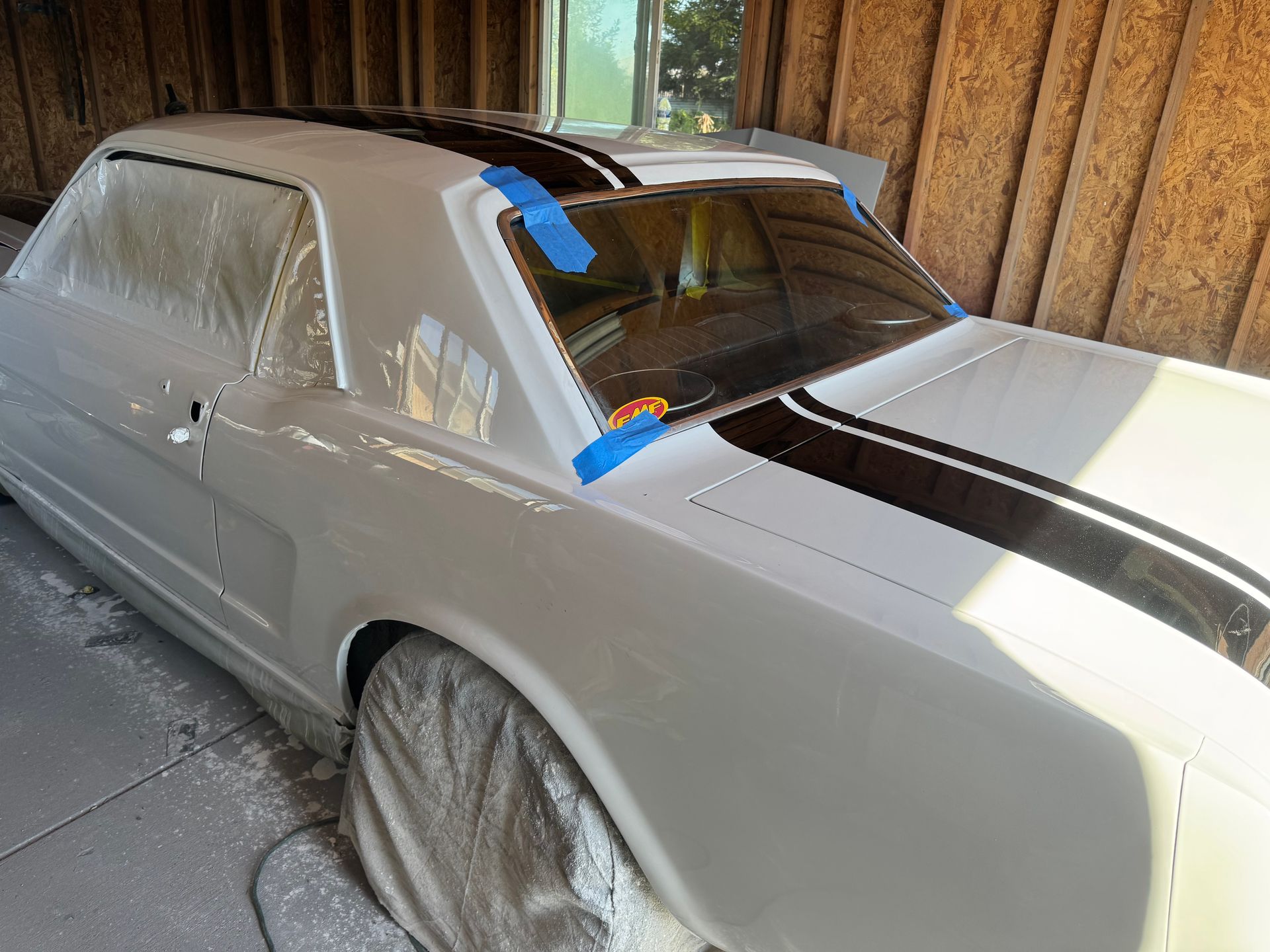 White classic car with black racing stripes being painted in a garage.