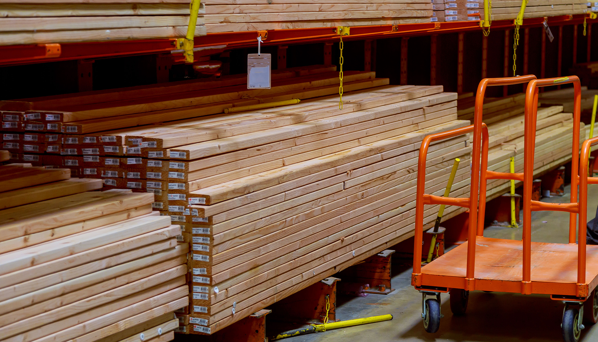 A man is pushing an orange cart in a warehouse filled with wood.