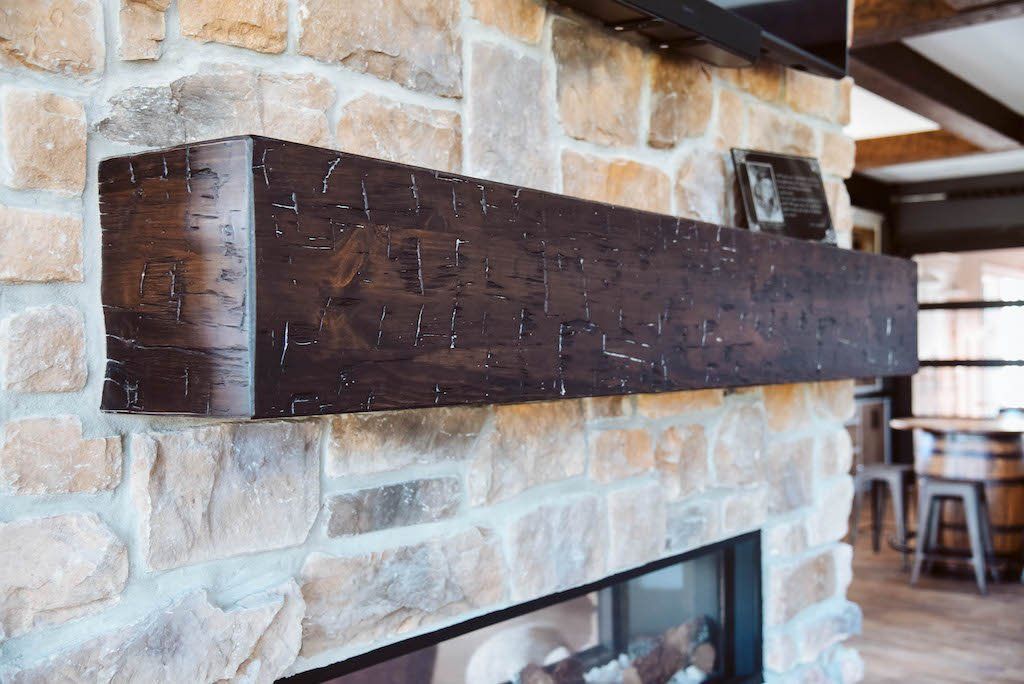 A fireplace with a wooden mantle and a stone wall.