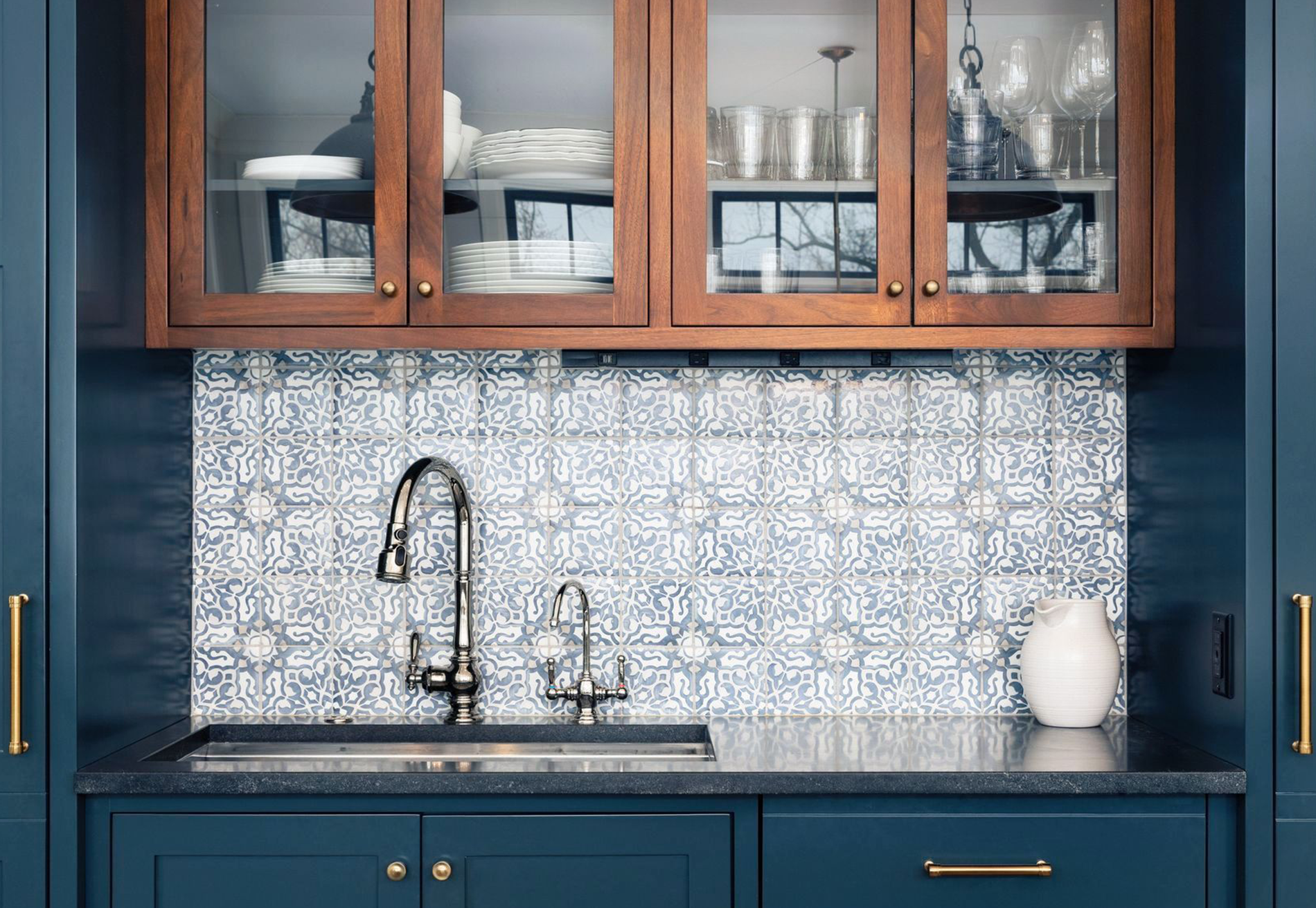 A kitchen with blue cabinets , a sink , and a glass cabinet.