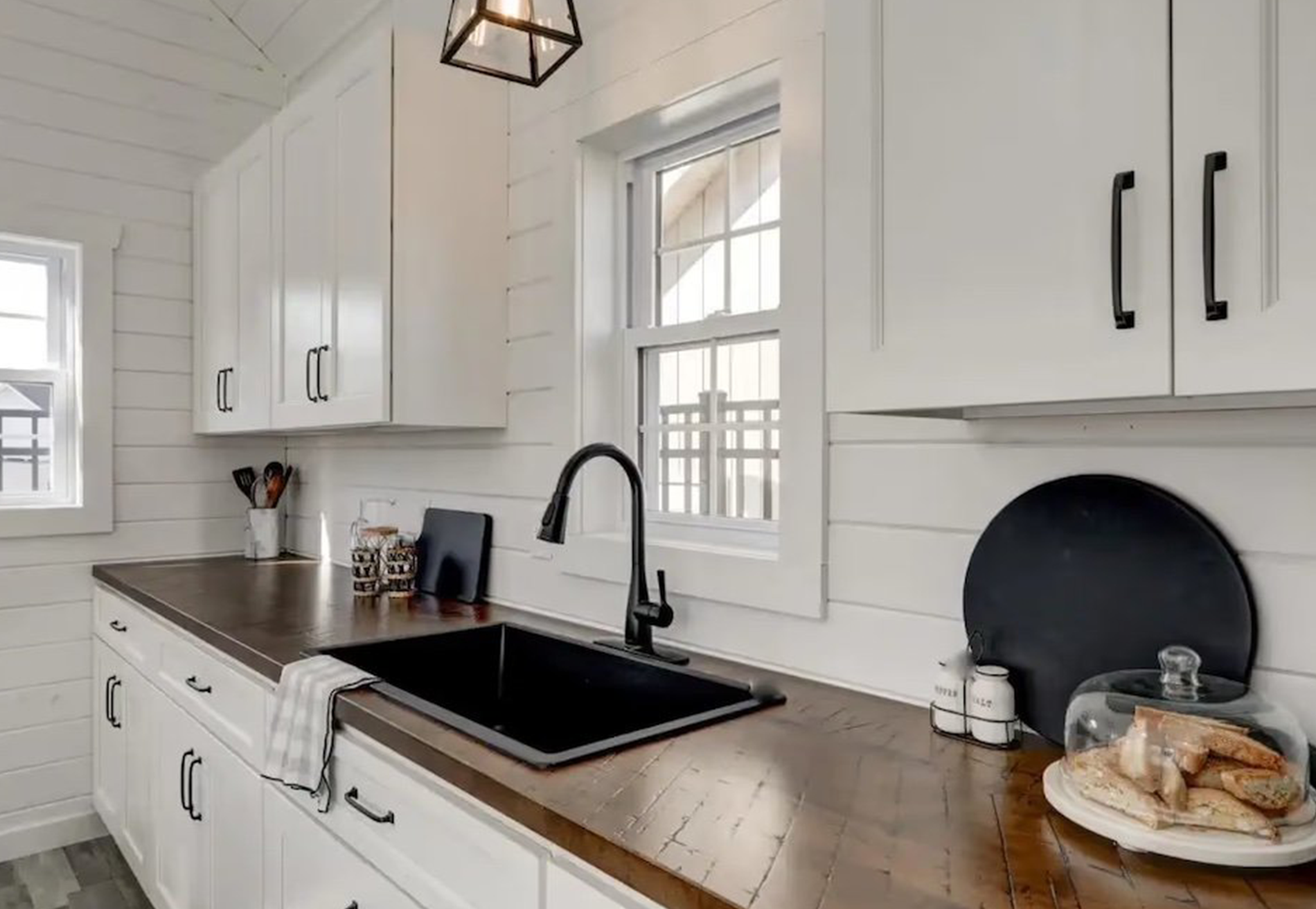 A kitchen with white cabinets , a black sink , and a window.