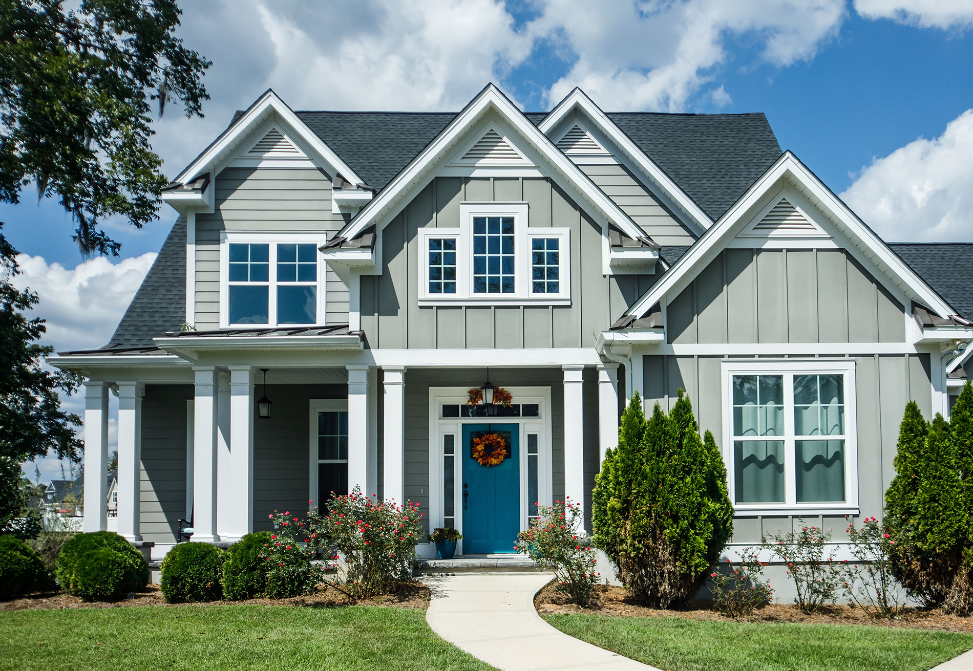 A large gray and white house with a blue door and a wreath on the front door.