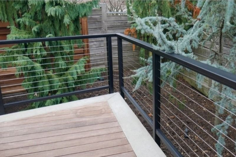 Wooden deck corner with black cable railing overlooking evergreen trees