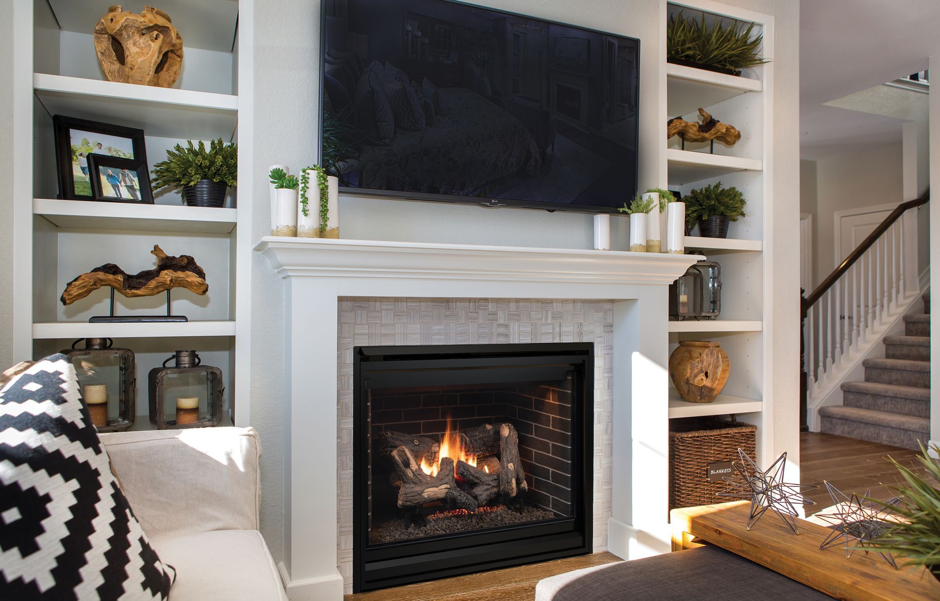 Living room with a fireplace, wall-mounted TV, built-in shelves, and a staircase in the background