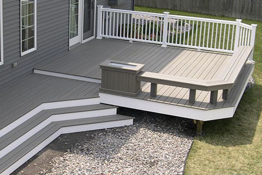 Backyard deck with white railing, gray steps, and built-in bench beside a house.