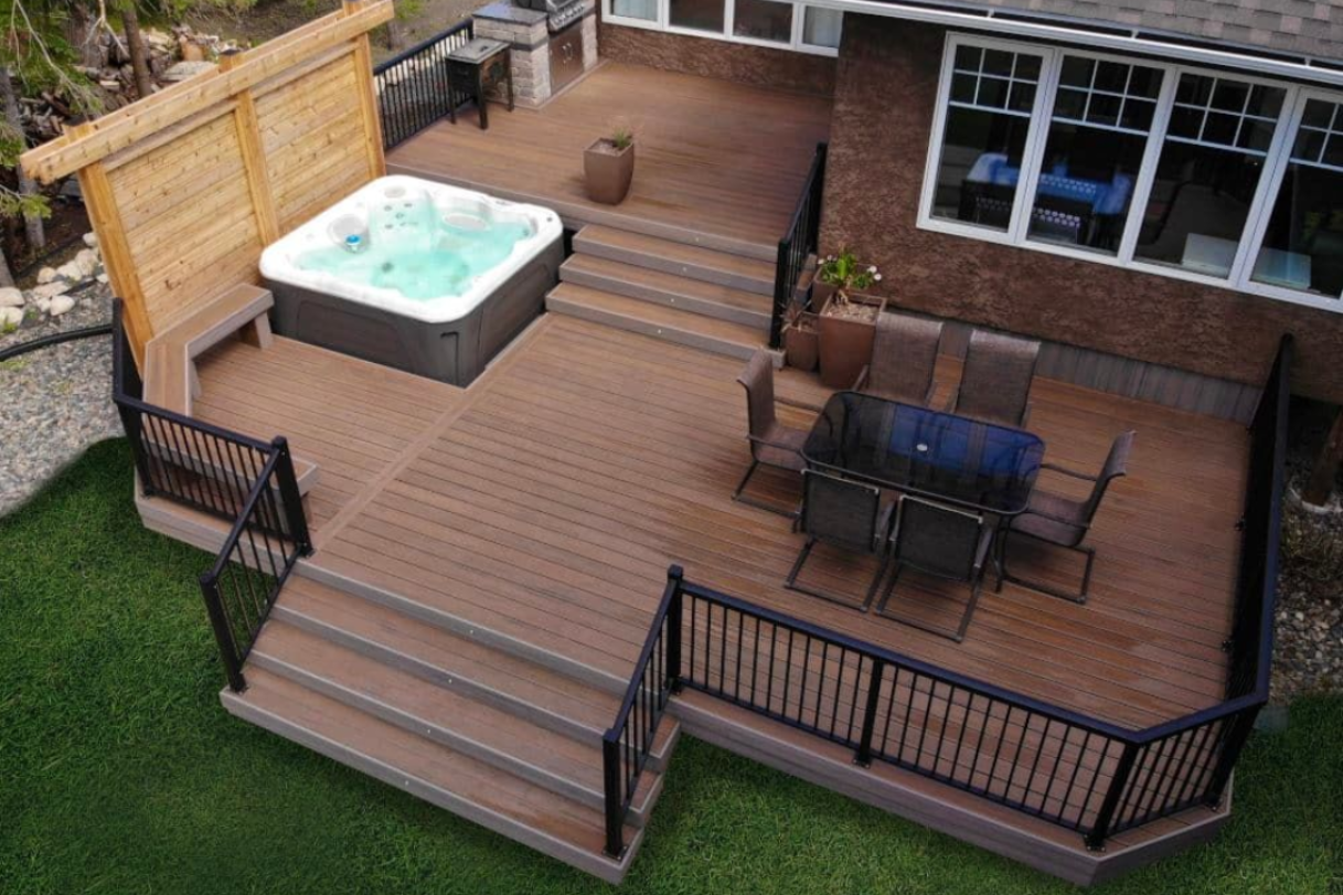 Backyard deck with hot tub, patio furniture, and black railing beside a brick house
