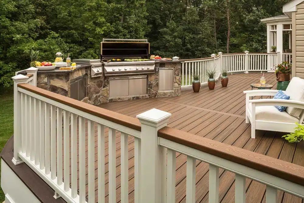 Spacious wooden deck with white railing, outdoor grill, and patio furniture beside a house and trees