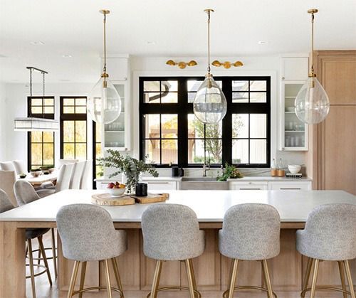 A kitchen with a large island and stools and a large window.
