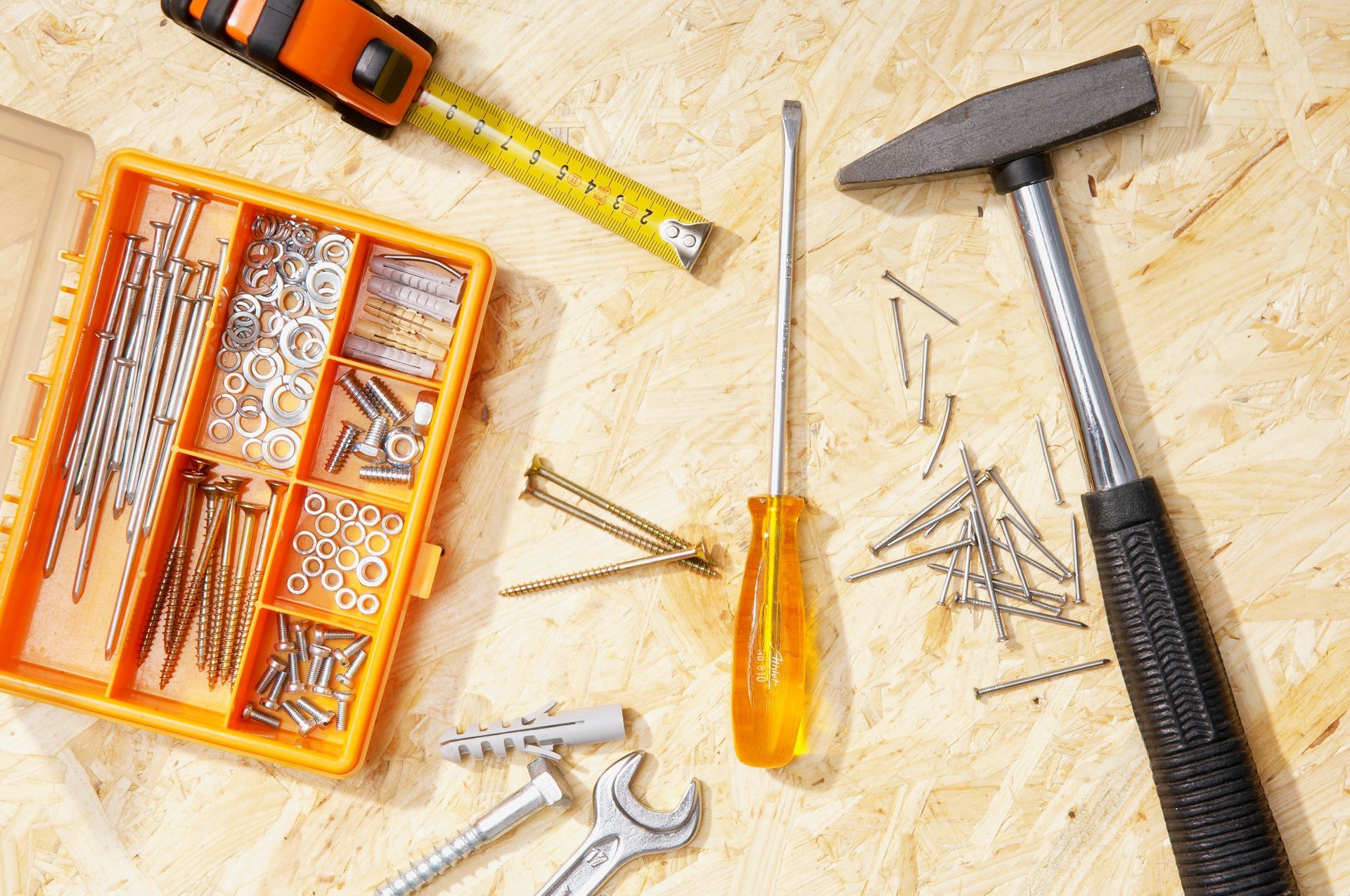 A hammer, screwdriver, tape measure, screws, and nails are on a wooden surface.