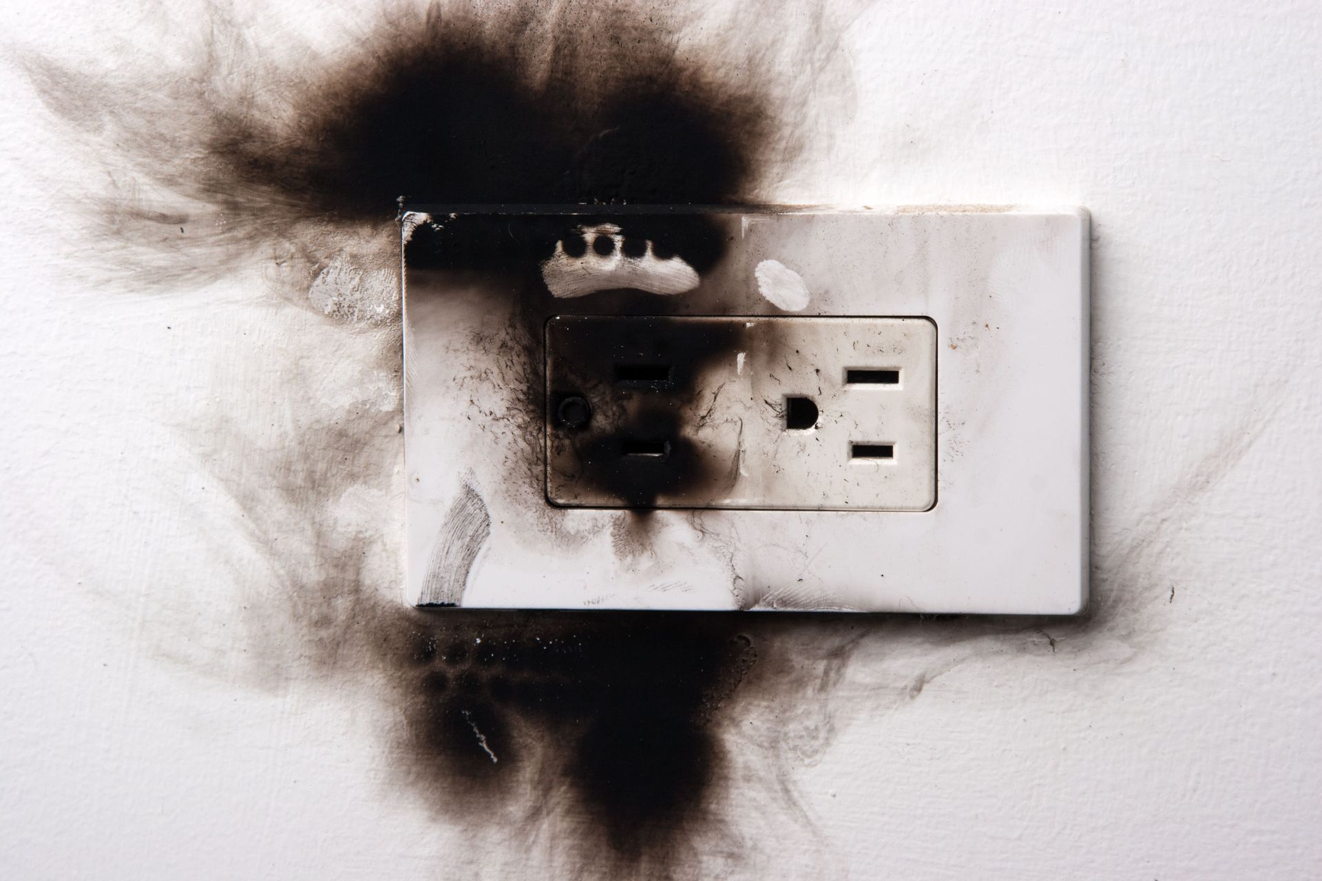 Burned electrical outlet on a wall, with black smoke stains around it