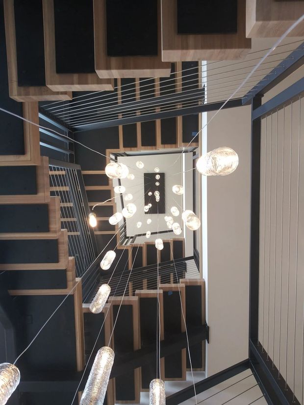 Upward view of a staircase with hanging pendant lights and dark wood railings in a modern interior.