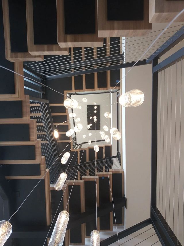 Upward view of a staircase with hanging pendant lights and dark wood railings in a modern interior.