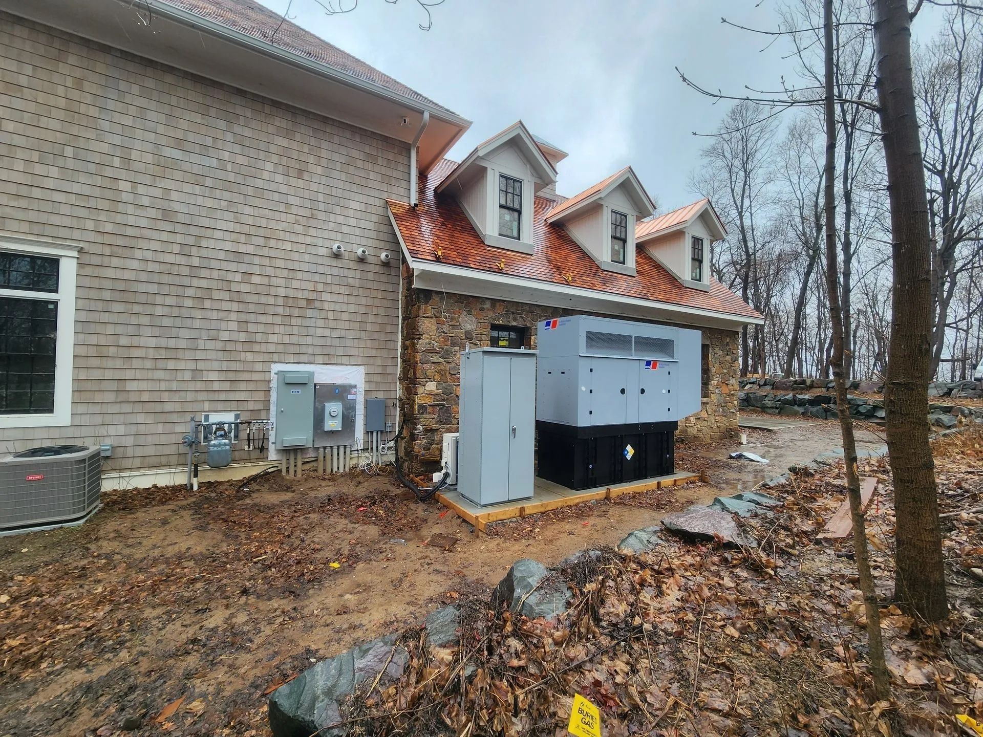 Exterior of a brick house with utility equipment and a large gray generator unit beside the wall