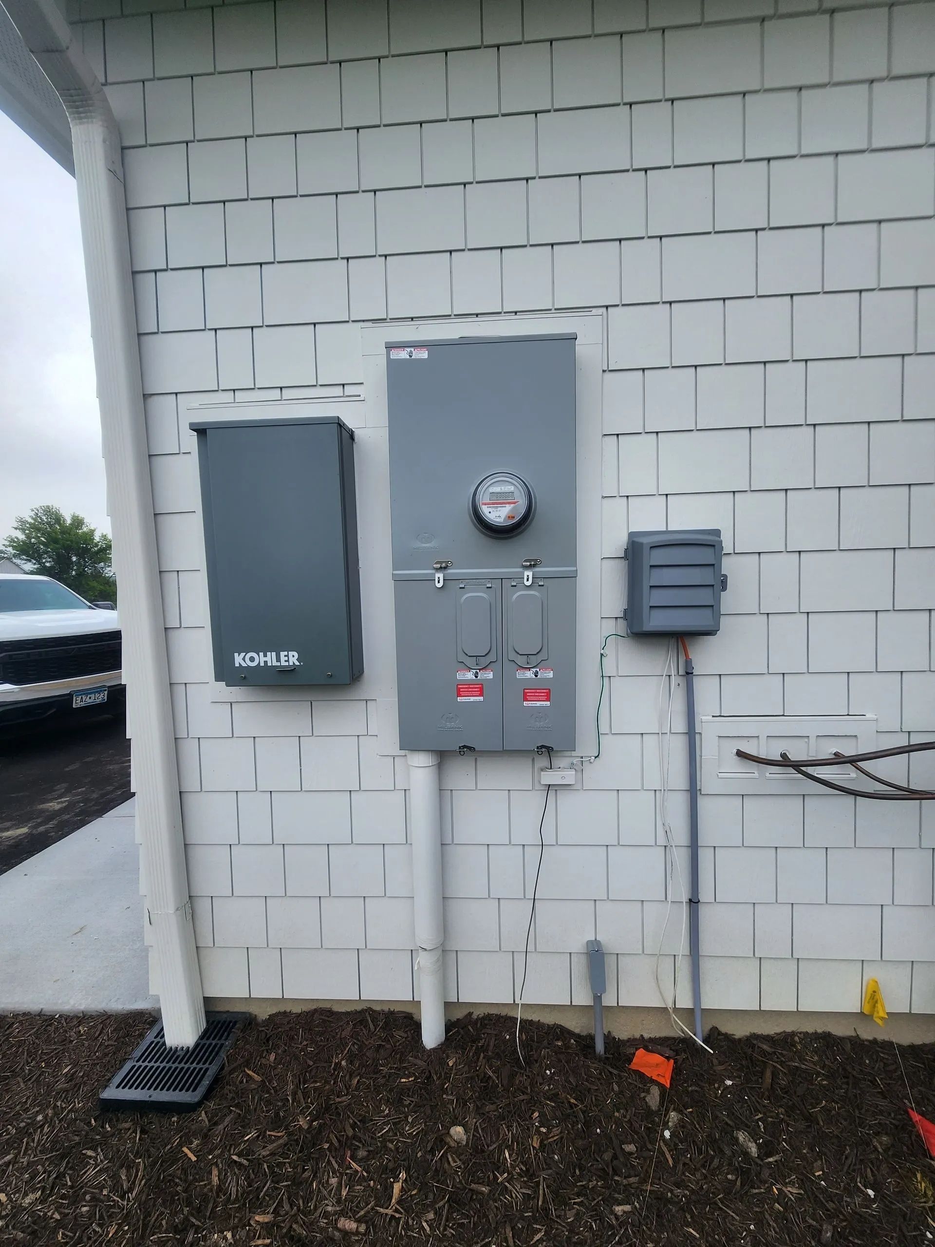 Exterior wall with electrical meter and gray utility boxes mounted on white cinder blocks.