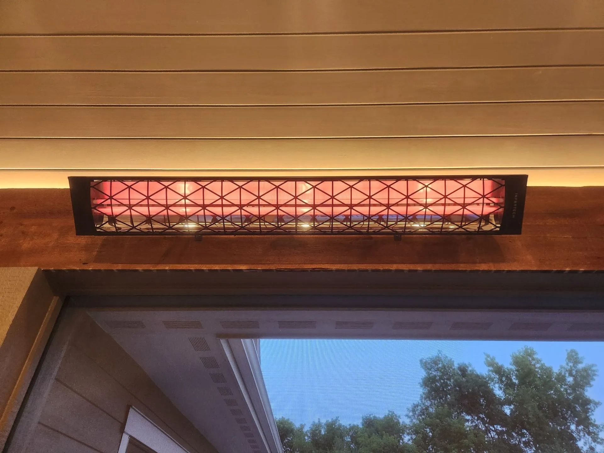 Outdoor heater above a window, glowing red under a wooden overhang at dusk