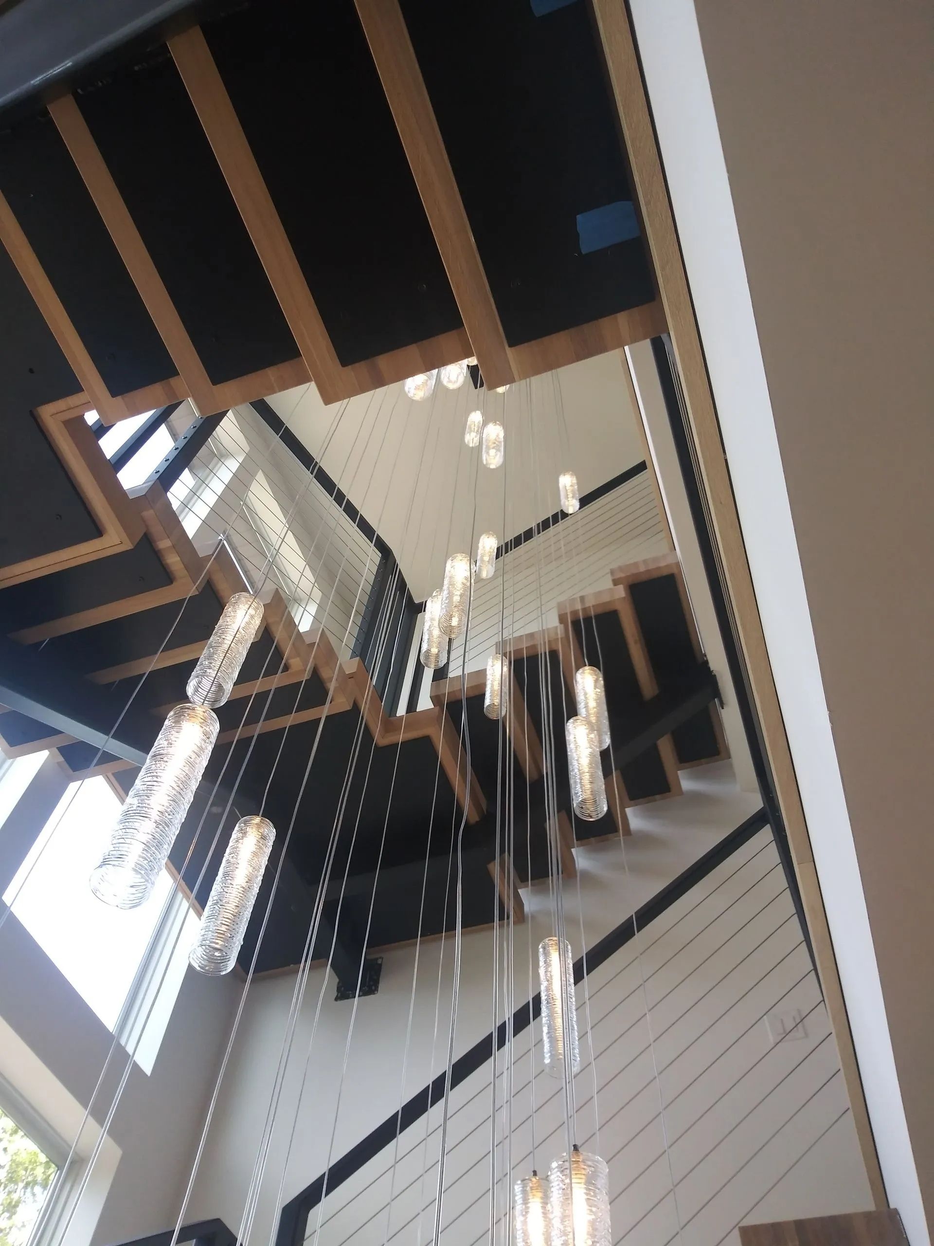 Modern interior with staircase, pendant lights, and tall windows reflected in a mirror.