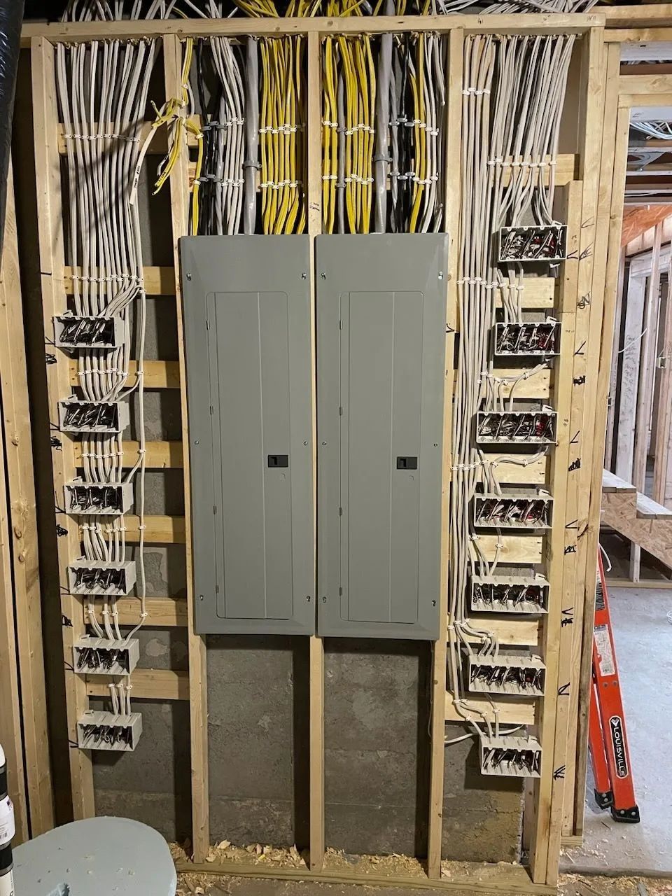 Electrical breaker panels amid exposed wiring in an unfinished wall during construction.