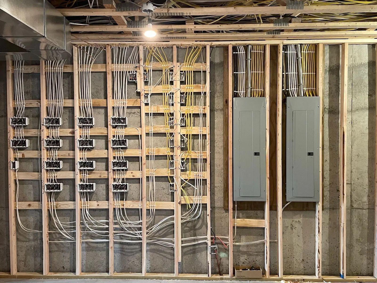 Basement electrical panel area with exposed wiring, studs, and two gray breaker boxes