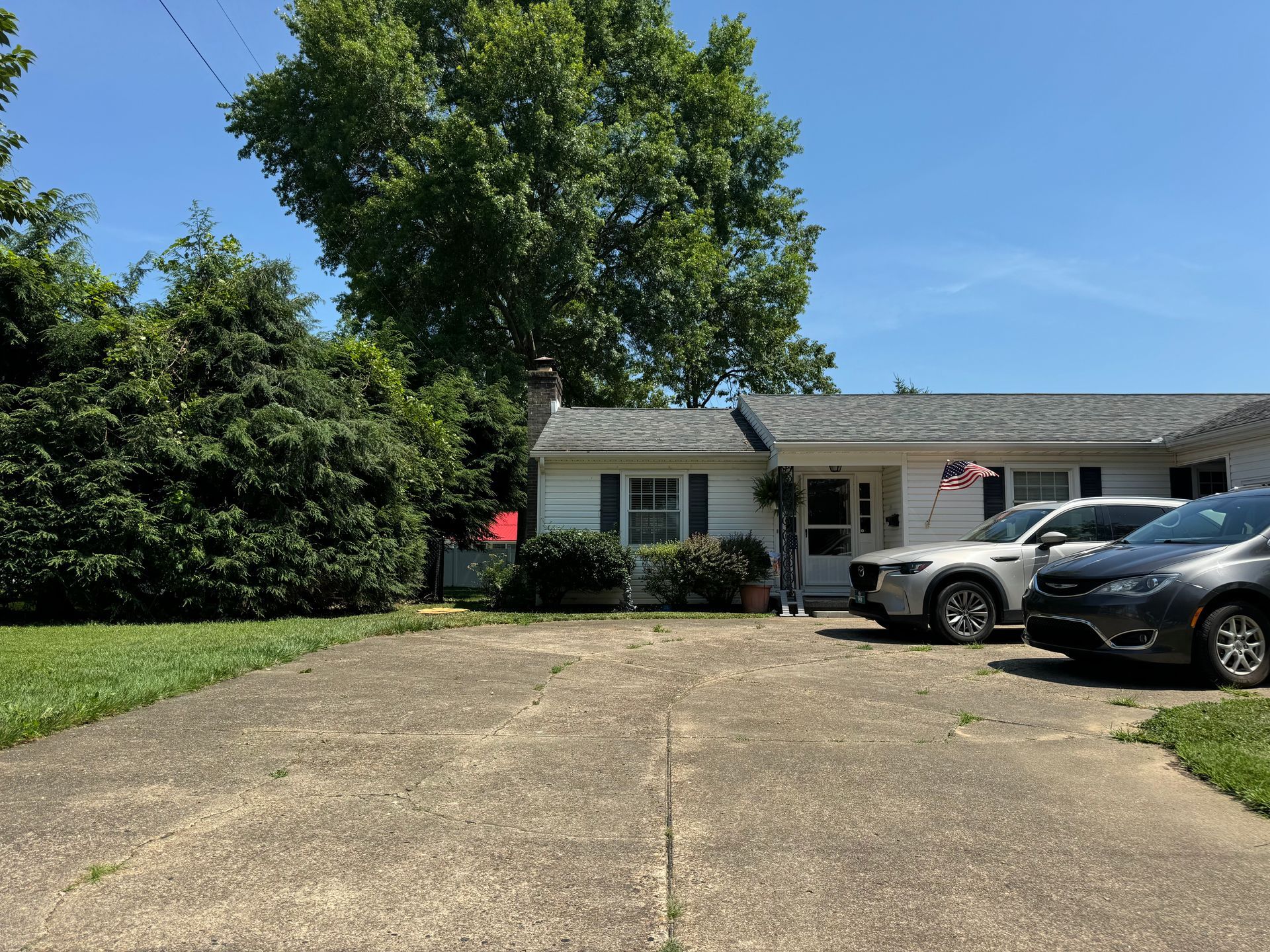 A white house with cars parked in front of it on a sunny day.