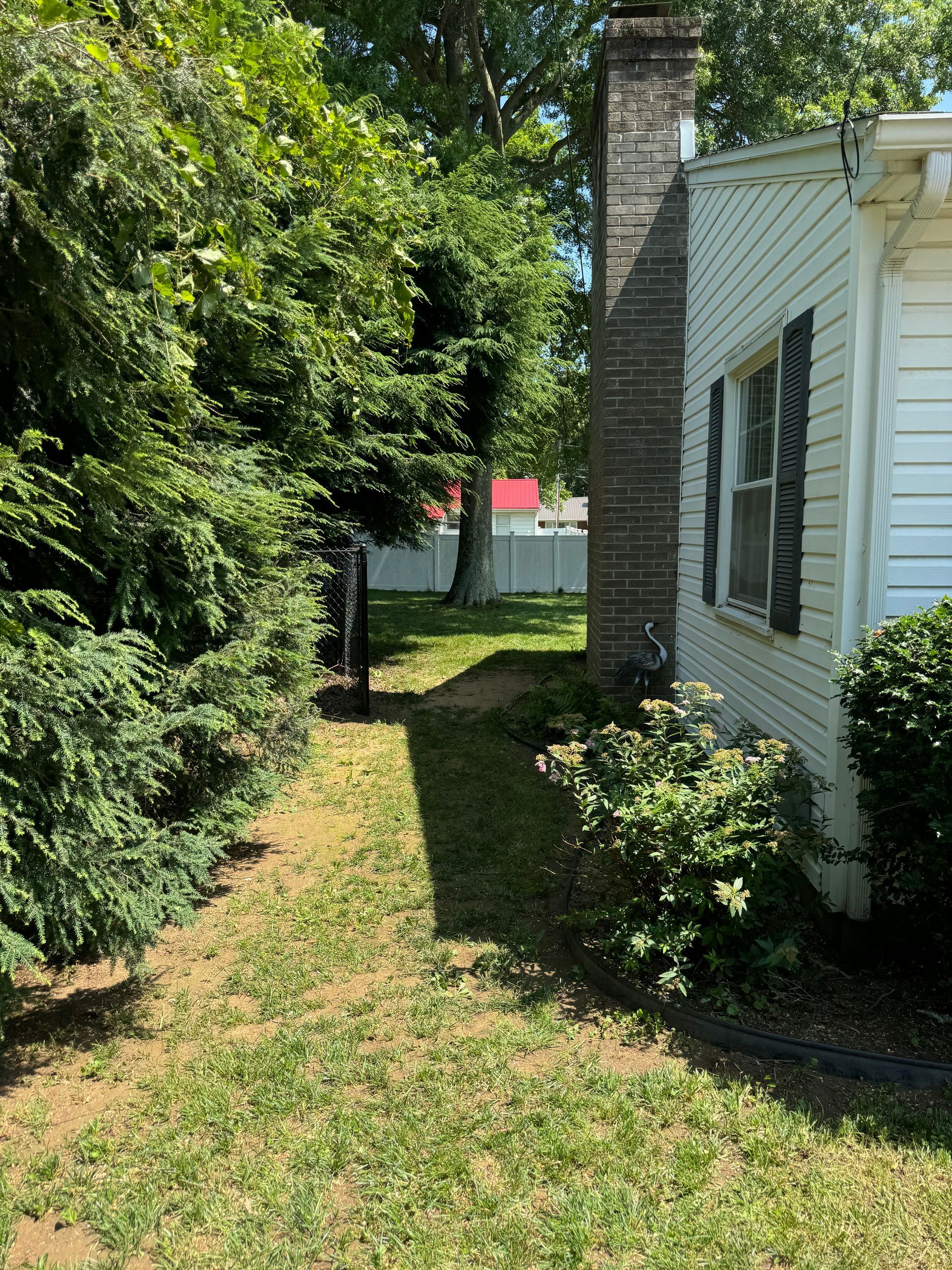 A white house with a brick chimney is surrounded by trees and bushes.