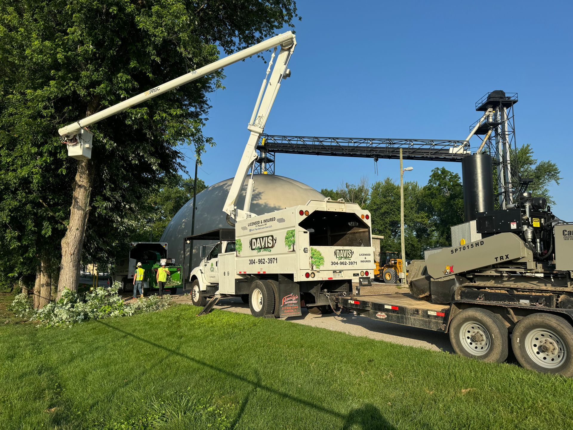A white truck with a crane on top of it is parked next to a tree.