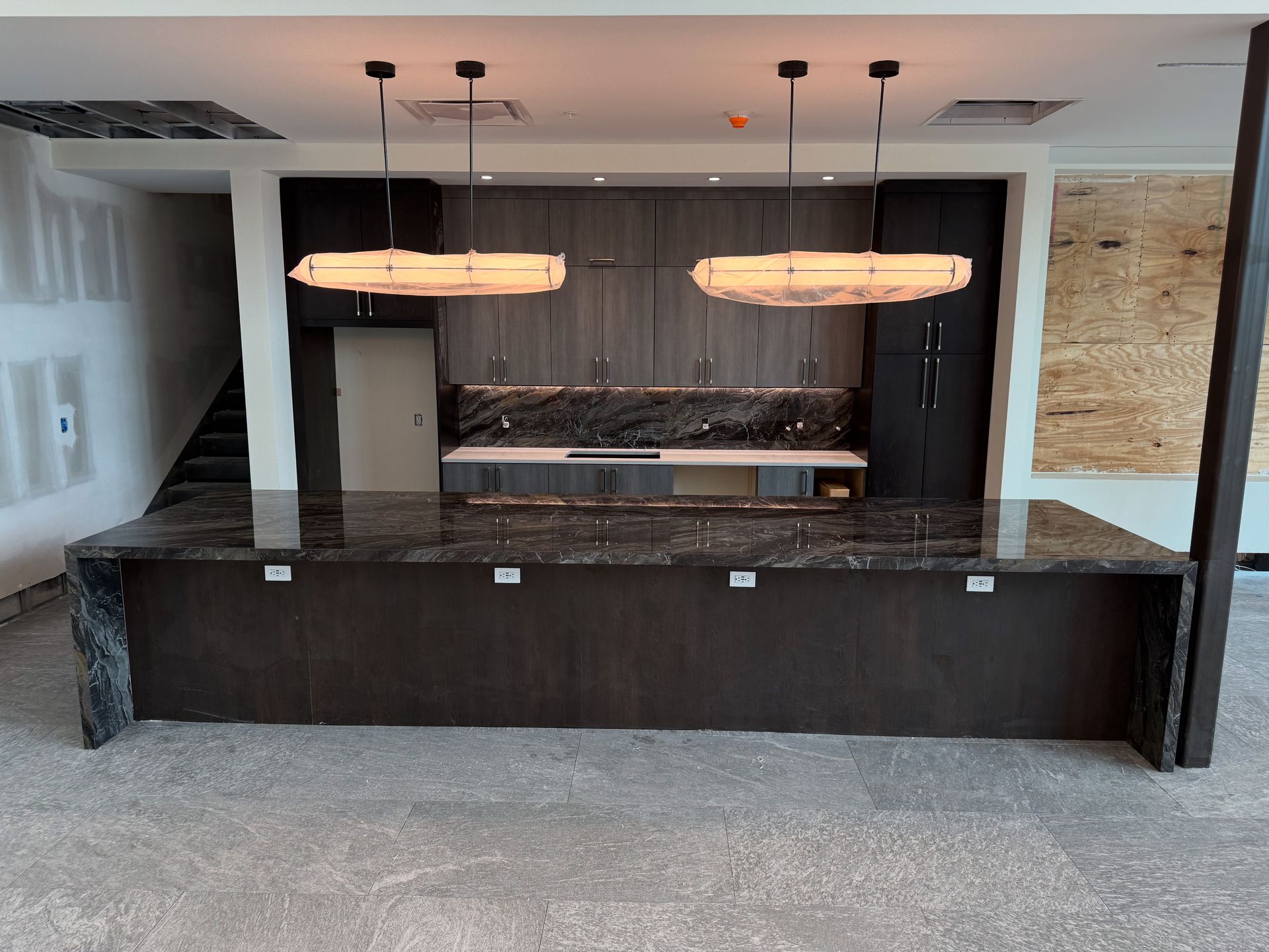 Modern kitchen with dark cabinets, marble island, and two pendant lights under construction