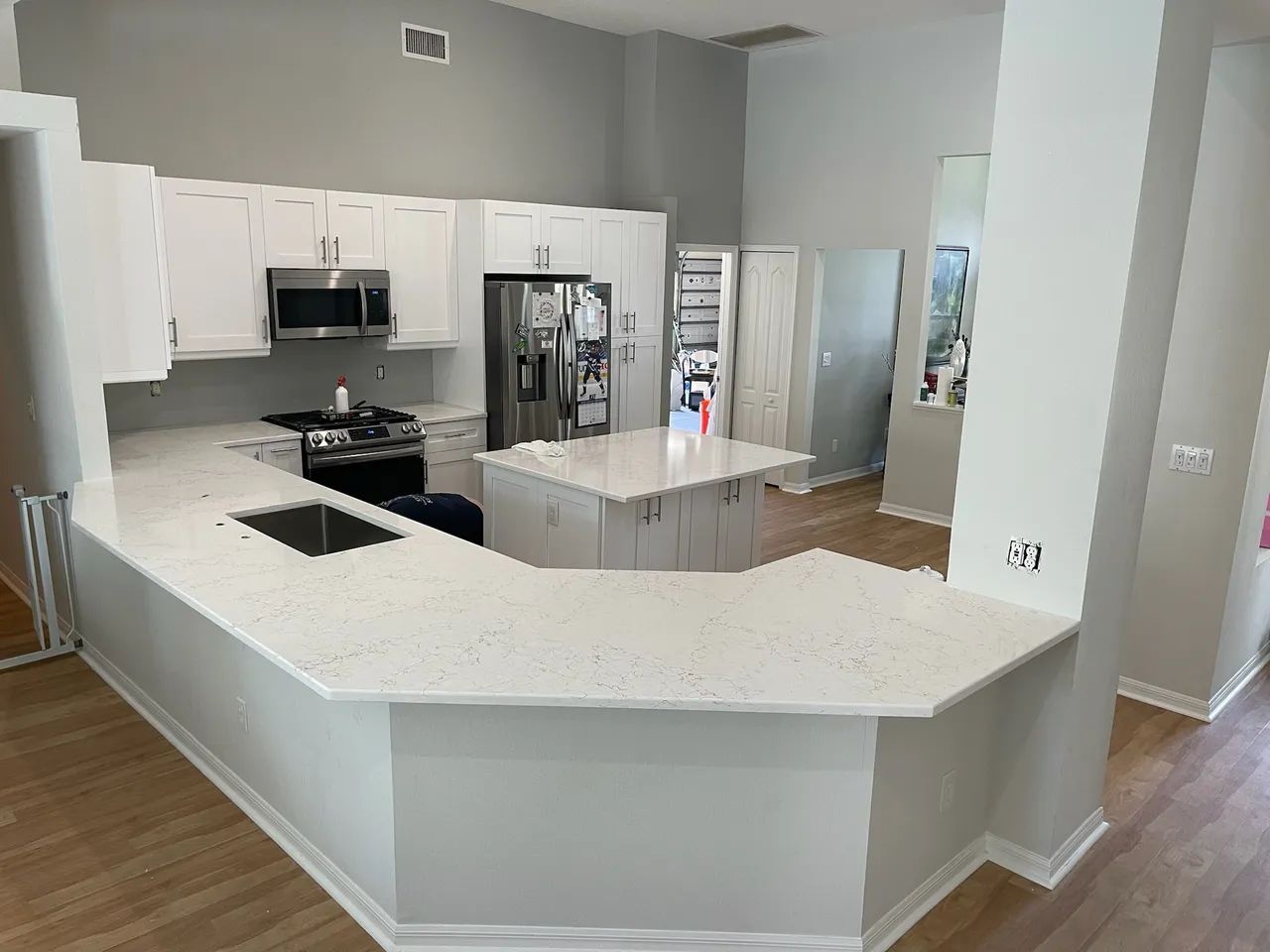 Empty modern kitchen with white cabinets, large island, stainless appliances, and light gray walls