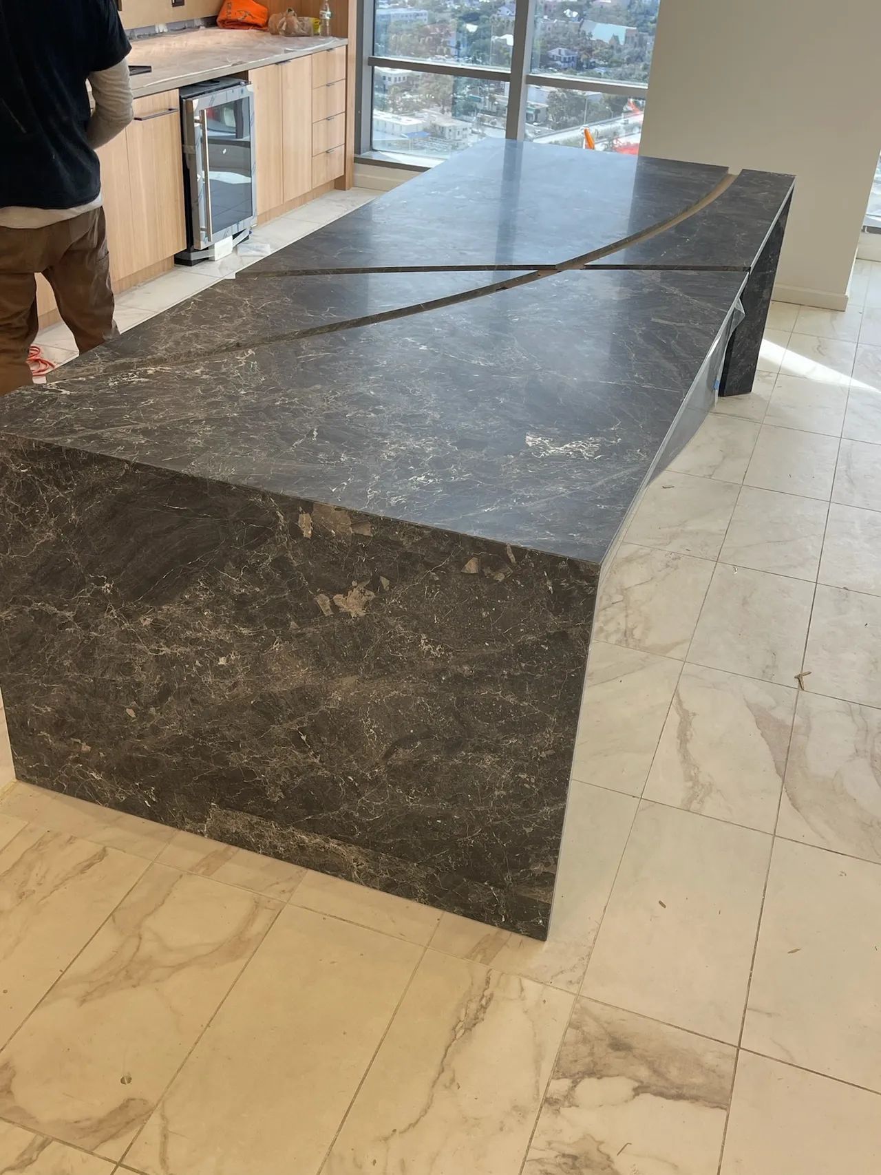 Large dark stone kitchen island or table in a bright room with white tile floor and glass doors