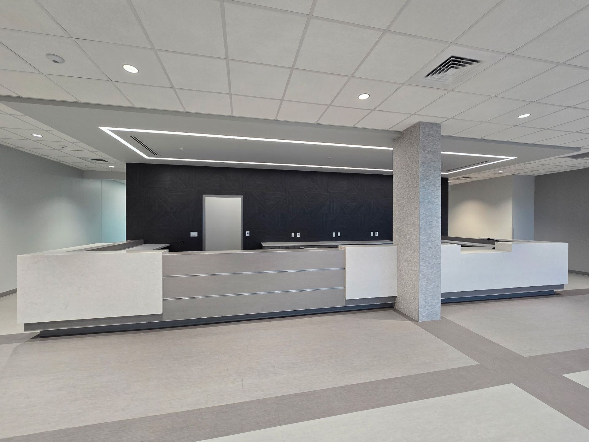 Empty modern lobby with white reception desks, dark accent wall, and gray tile floor