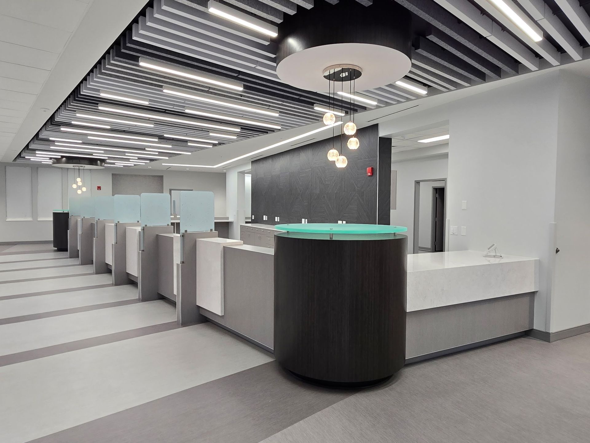 Modern office lobby with gray cubicles, a reception desk, and striped ceiling lights