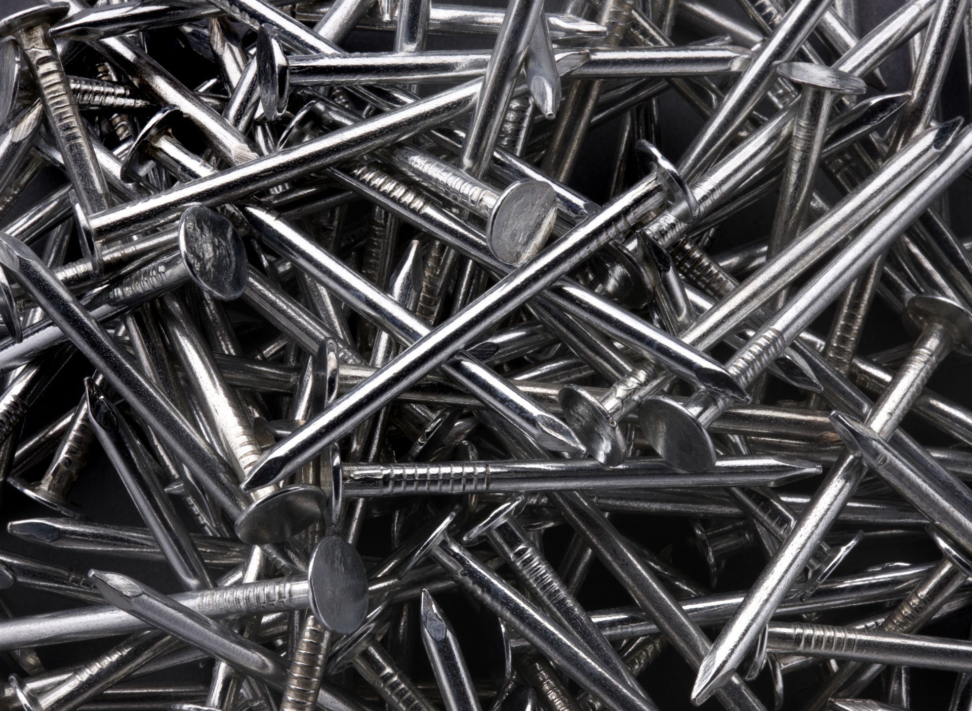 Pile of shiny metal nails scattered in a heap on a dark background