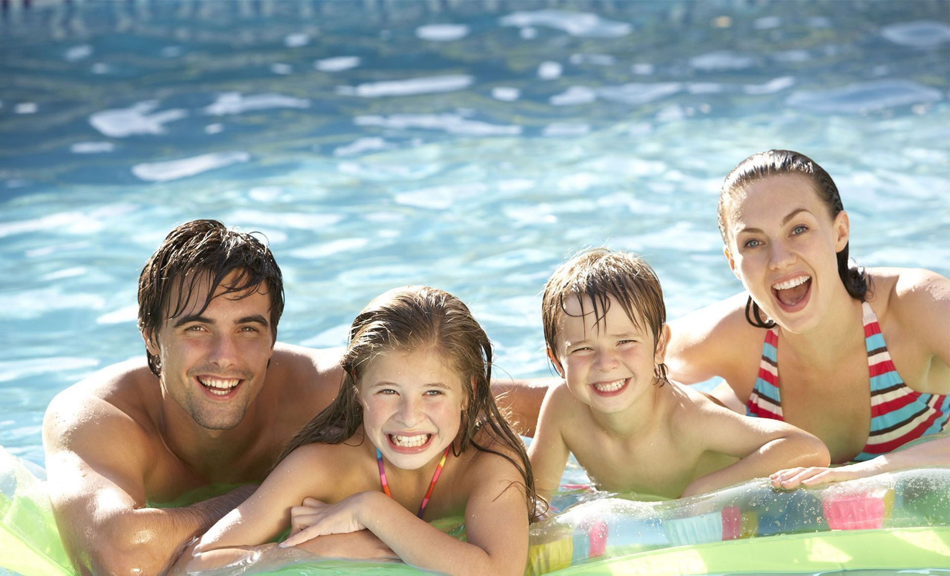 Family smiles and enjoys a swim in a pool on a sunny day.